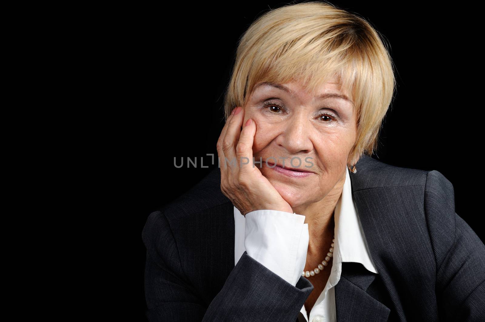 Portrait of an elderly woman (70+) in a business suit against a dark background close-up