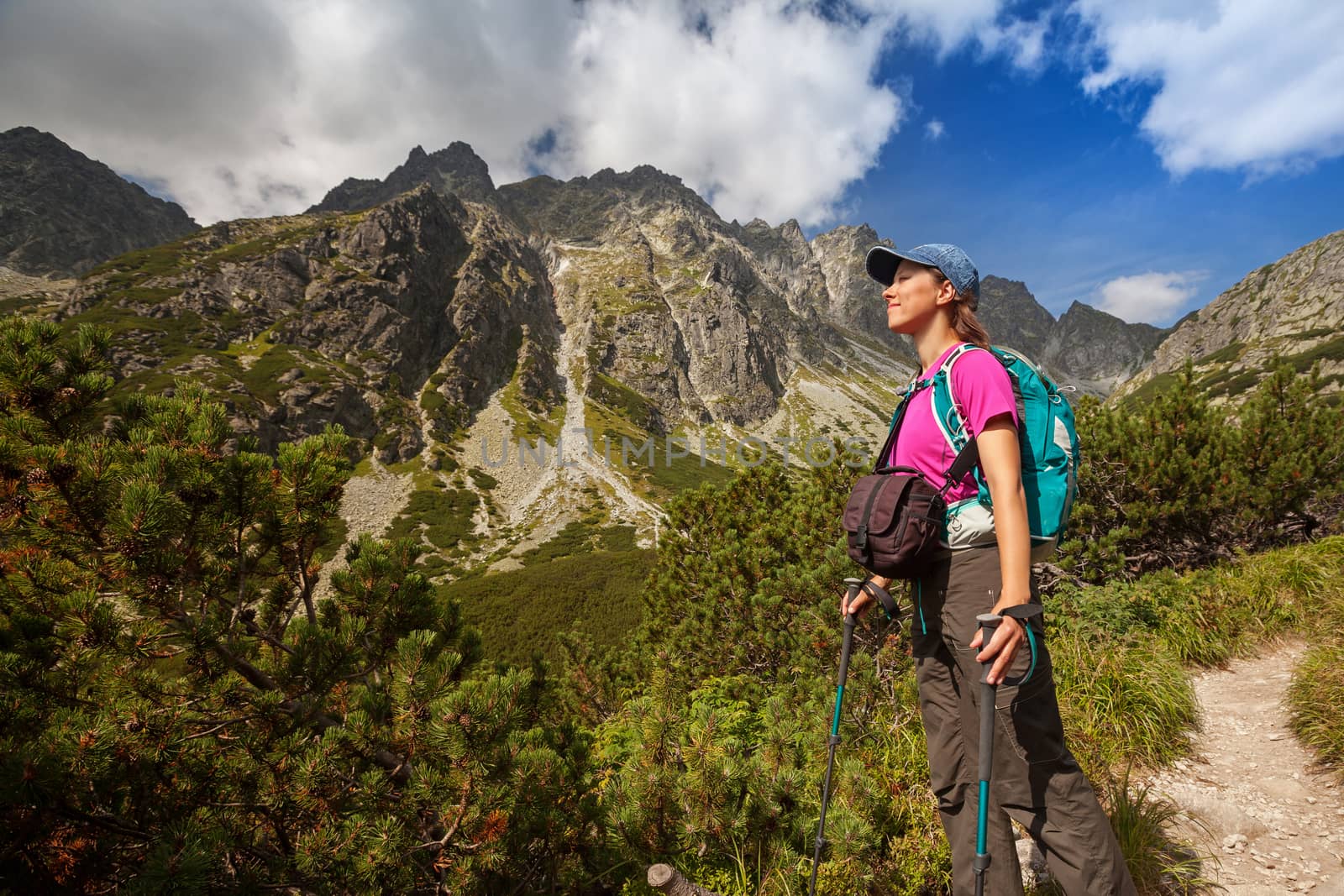 Happy woman with backpack standing and looking on high rocky peaks near Zelene Pleso in Tatra Mountains, Slovakia, Europe
