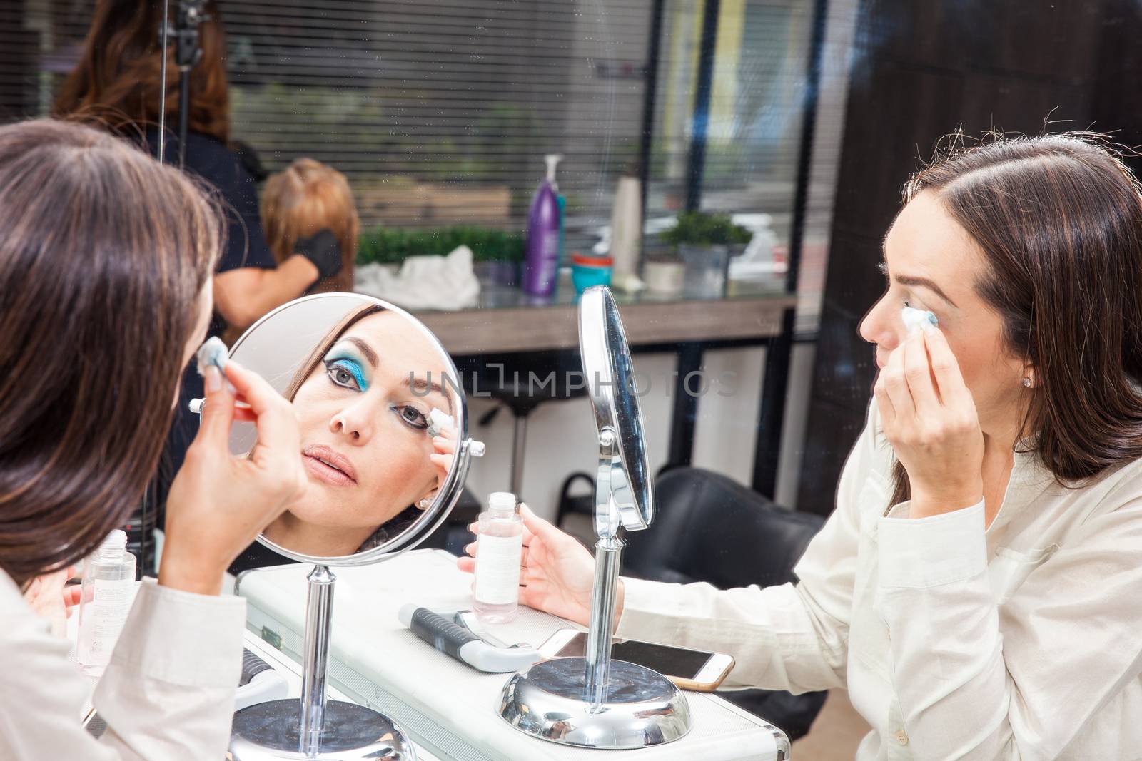 White woman removing makeup in front of mirror at beauty salon