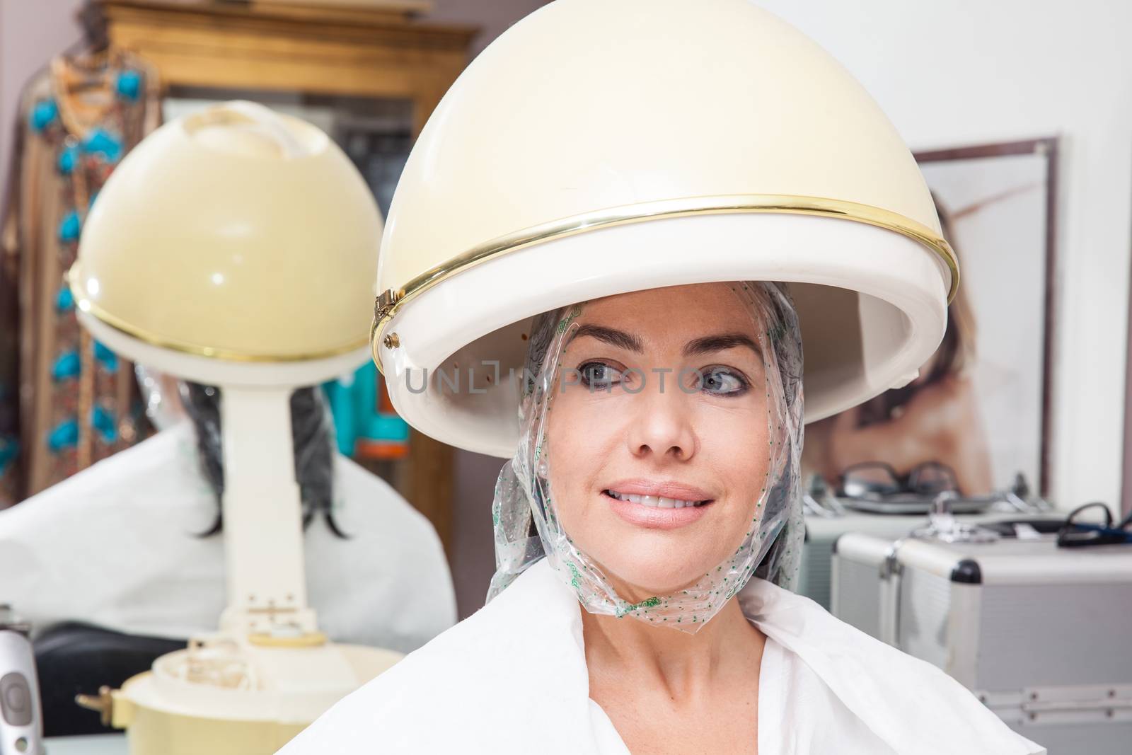 Woman under a professional hair steamer with a hair treatment