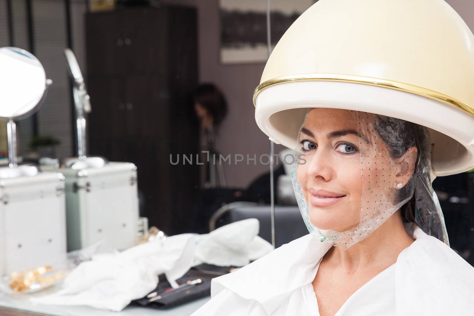 Woman under a professional hair steamer with a hair treatment