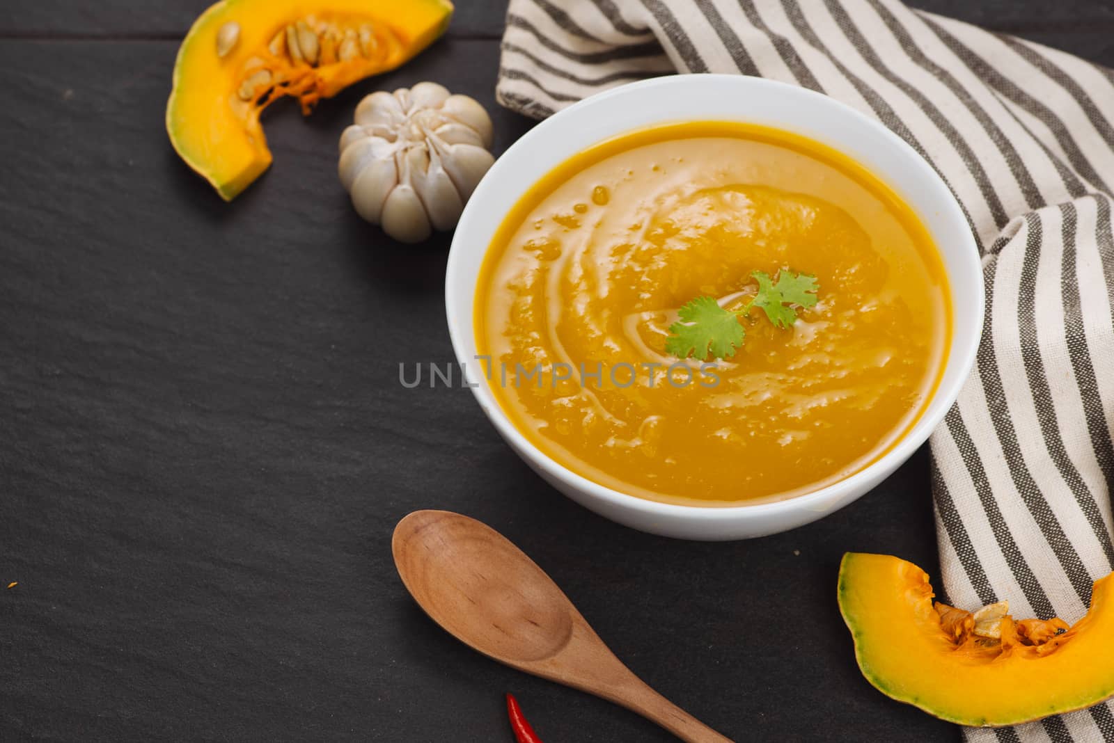 Pumpkin soup in a bowl with fresh pumpkins, garlic and parsley h by makidotvn