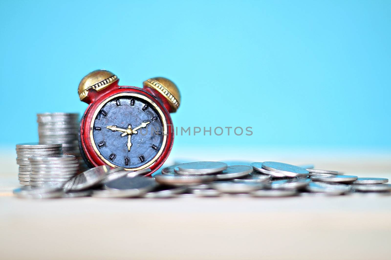 Miniature clock and coins stack on desk table by sureeporn