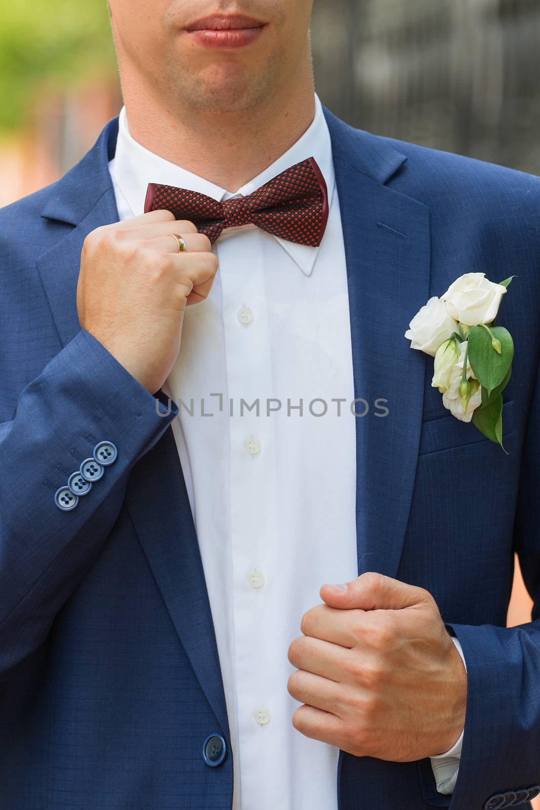 Stylish groom straightens a tie . Closeup of the clothed in blue jacket and white shirt at the park on their wedding day