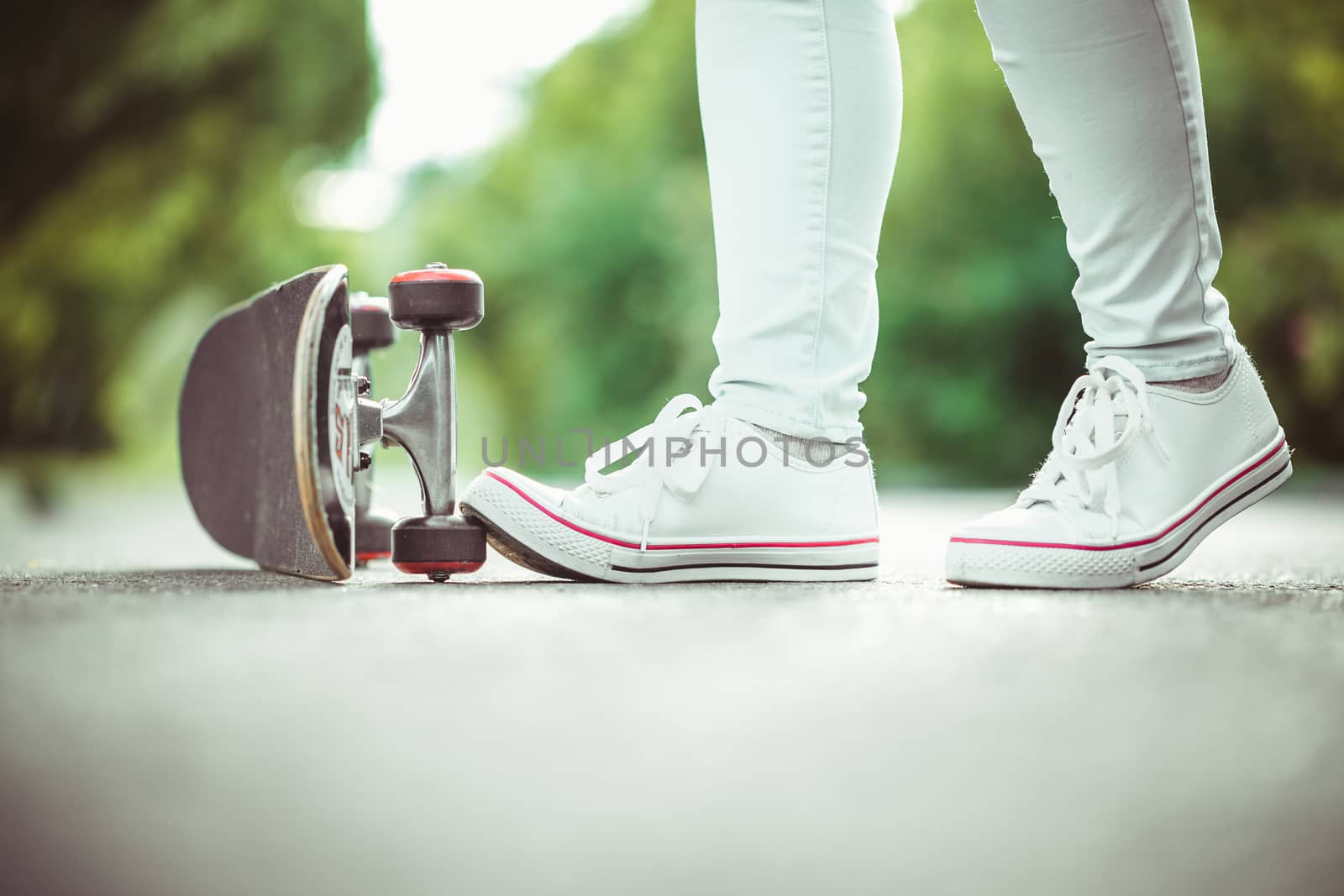 female feet in white sneakers and skateboard close up