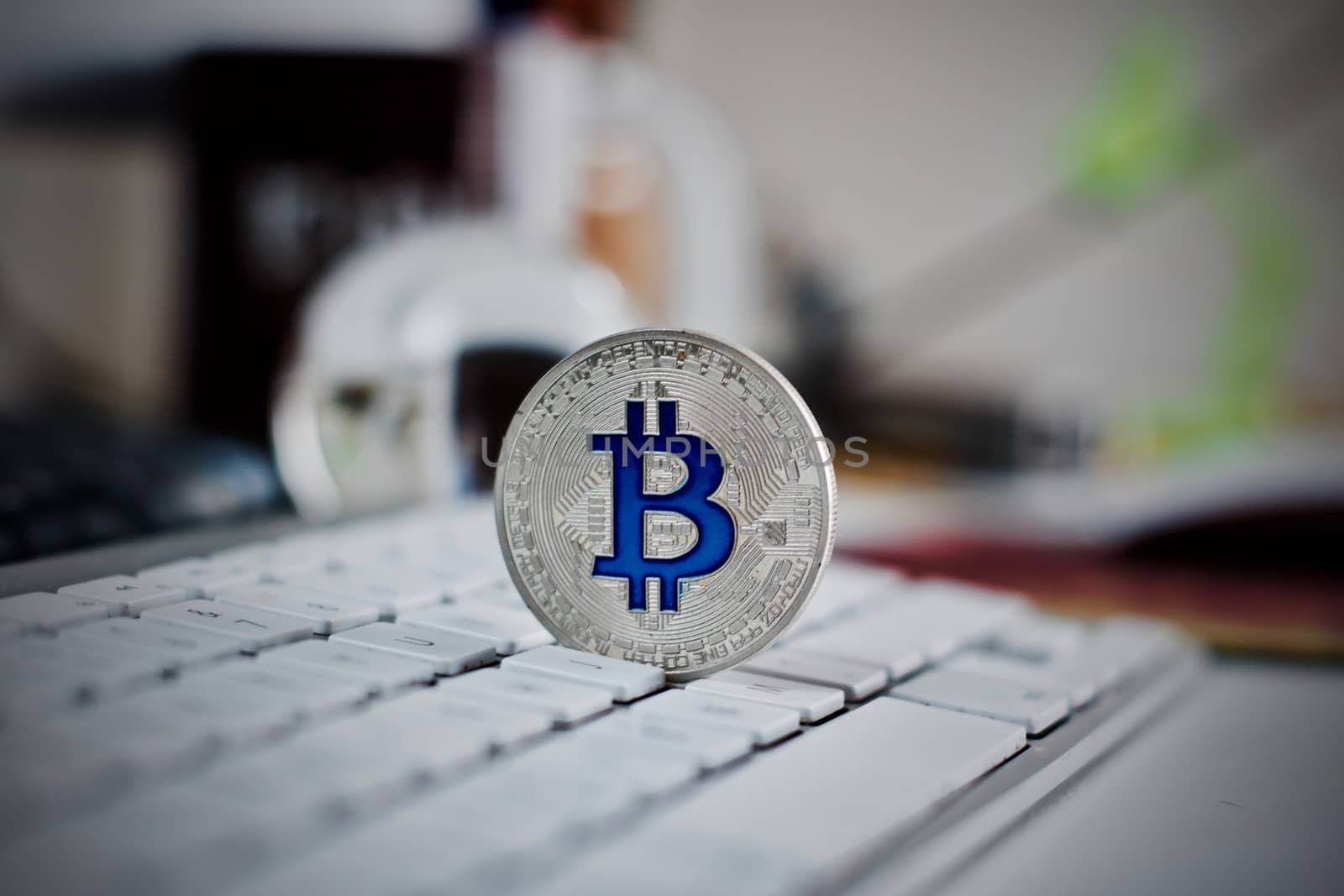 Digital currency physical metal bitcoin coin on the white keyboard near glass ball.