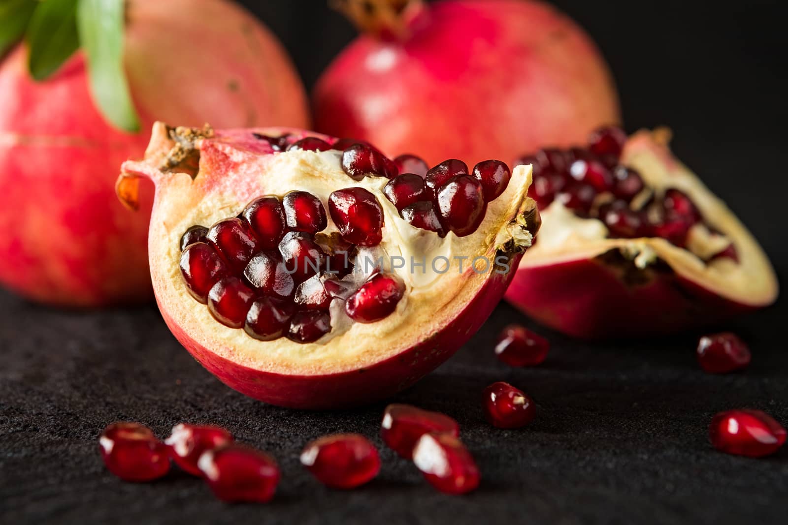 Closeup of half pomegranate fruit and seeds on a black textured background