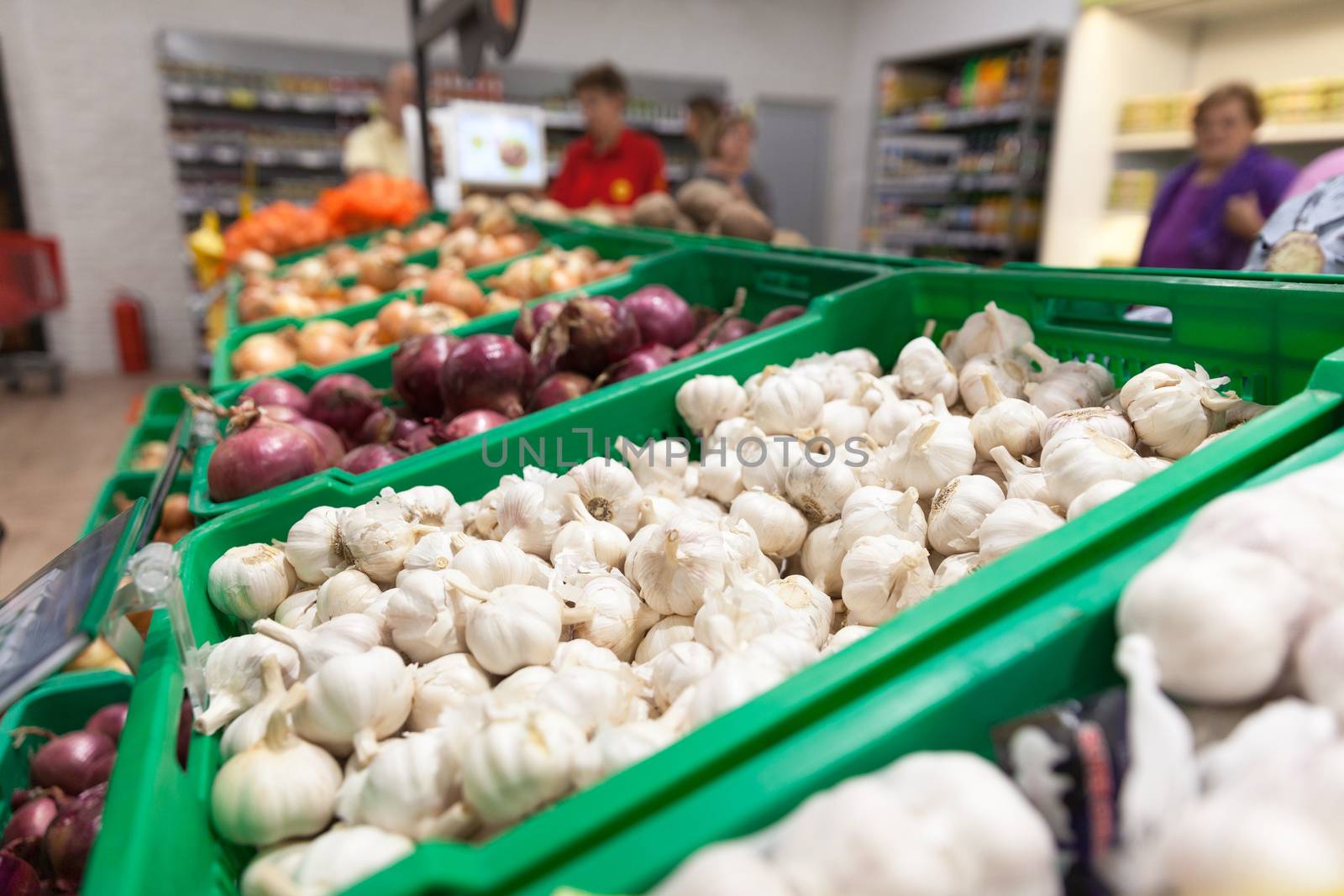 Garlic on supermarket vegetable shelf, blurred buyers in the background