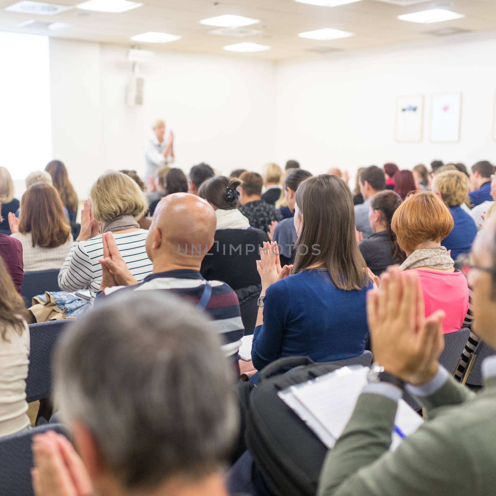 Life coaching symposium. Female speaker giving interactive motivational speech at entrepreneurship workshop. Audience in conference hall. Rear view of unrecognized participant.