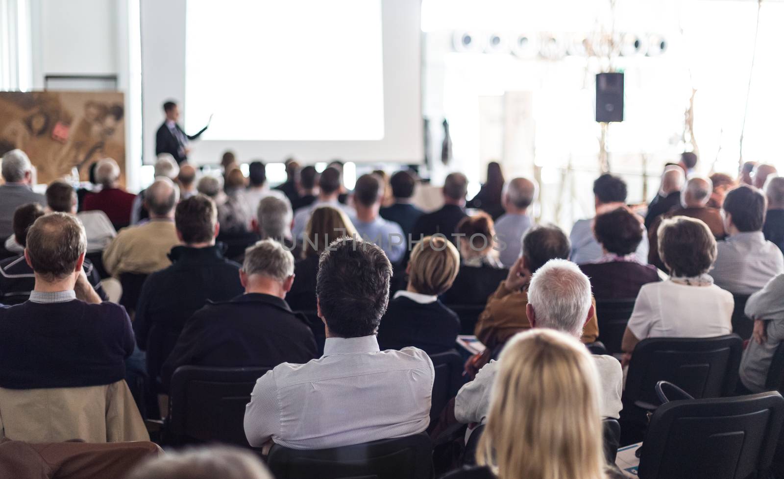 Speaker giving a talk in conference hall at business event. Audience at the conference hall. Business and Entrepreneurship concept. Focus on unrecognizable man in the audience.