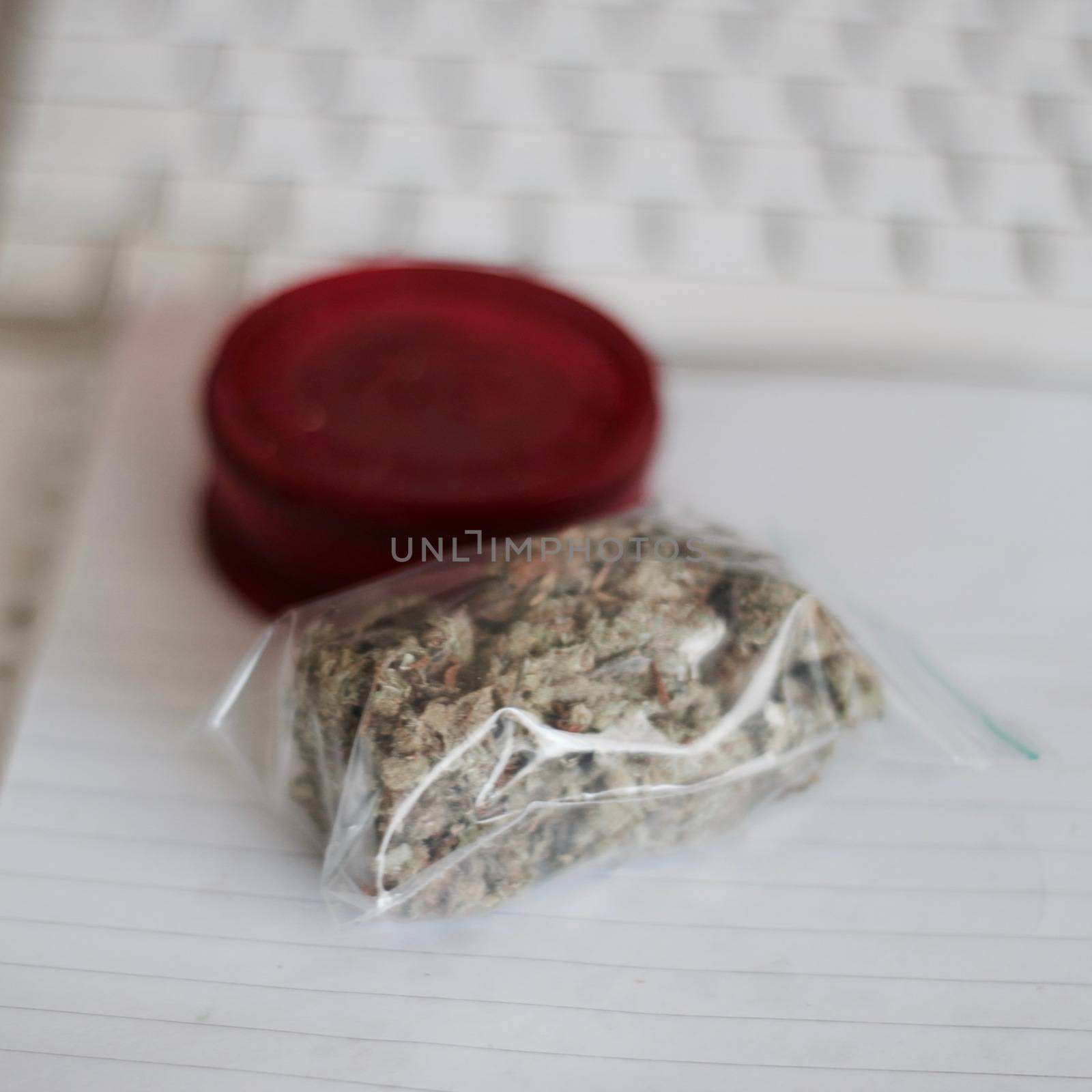 Red grinder, marijuana in big transparent bag near white computer keyboard.