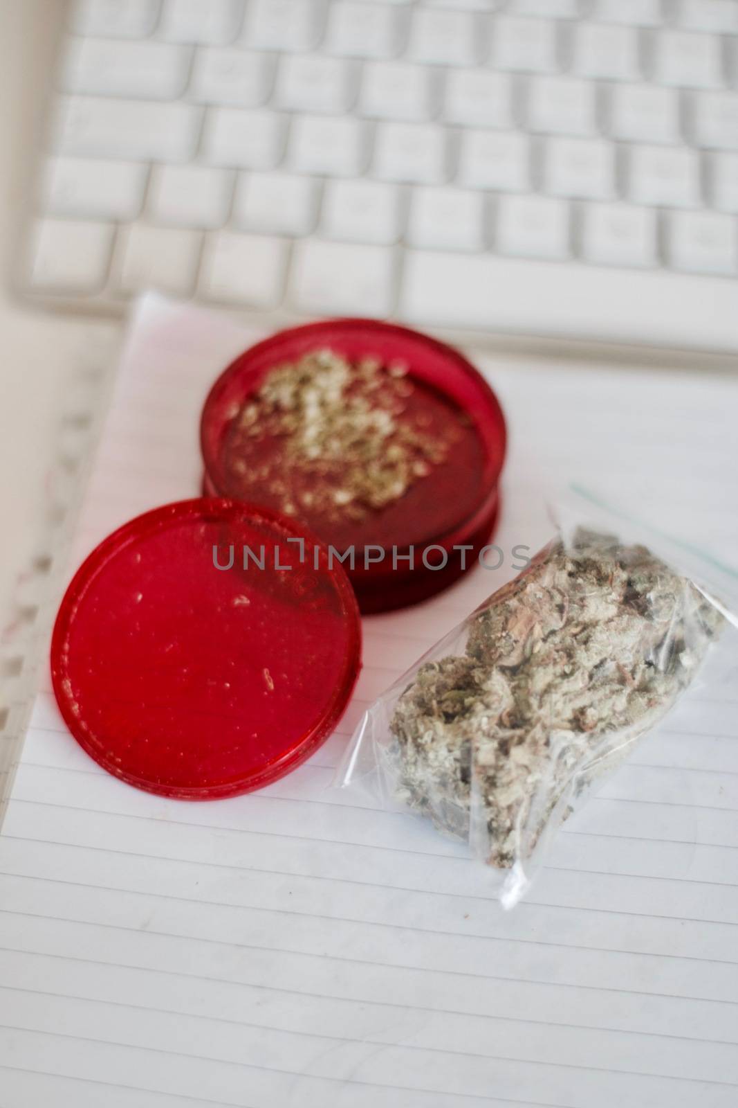 Red grinder, marijuana in big transparent bag near white computer keyboard.