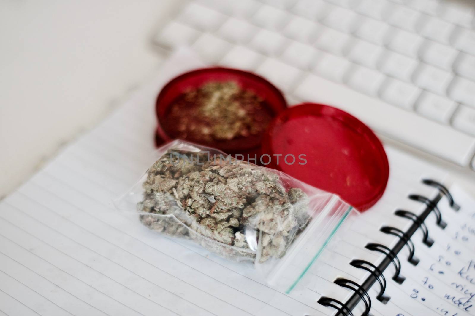 Red grinder, marijuana in big transparent bag near white computer keyboard.