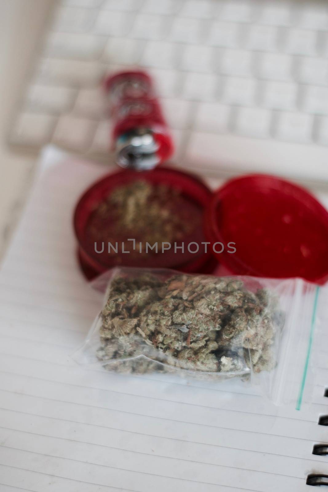 Red grinder, marijuana in big transparent bag near white computer keyboard.