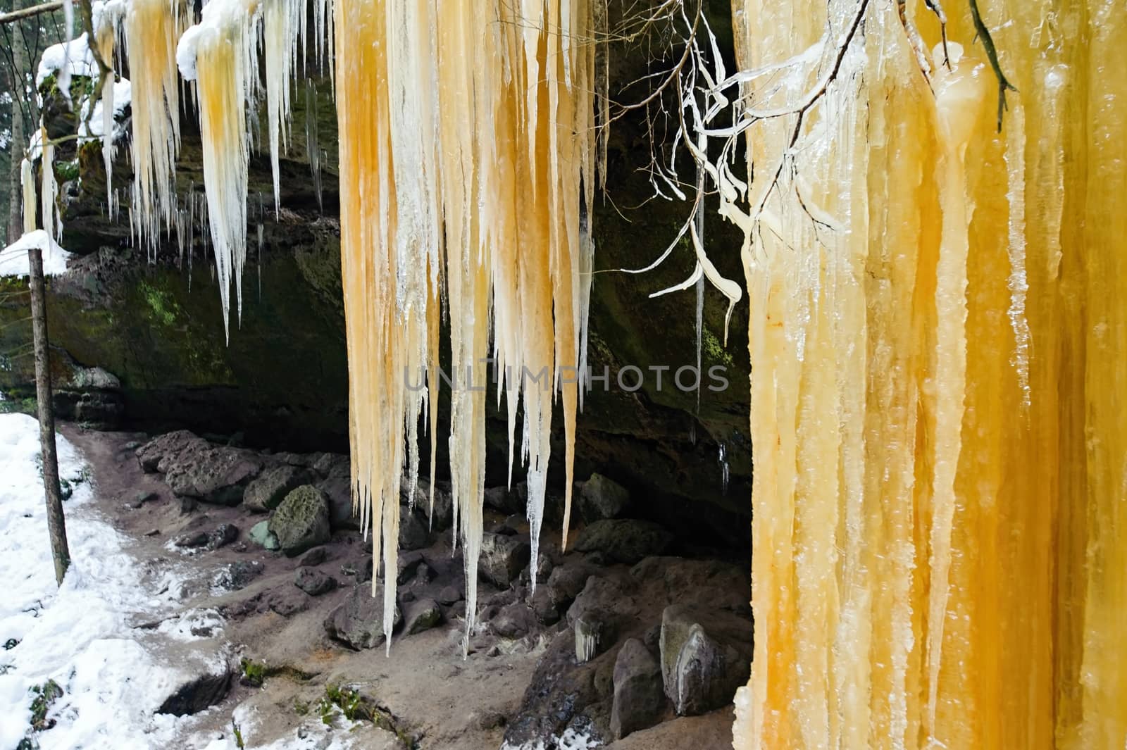 Frozen waterfalls on the rock, orange colored and snow