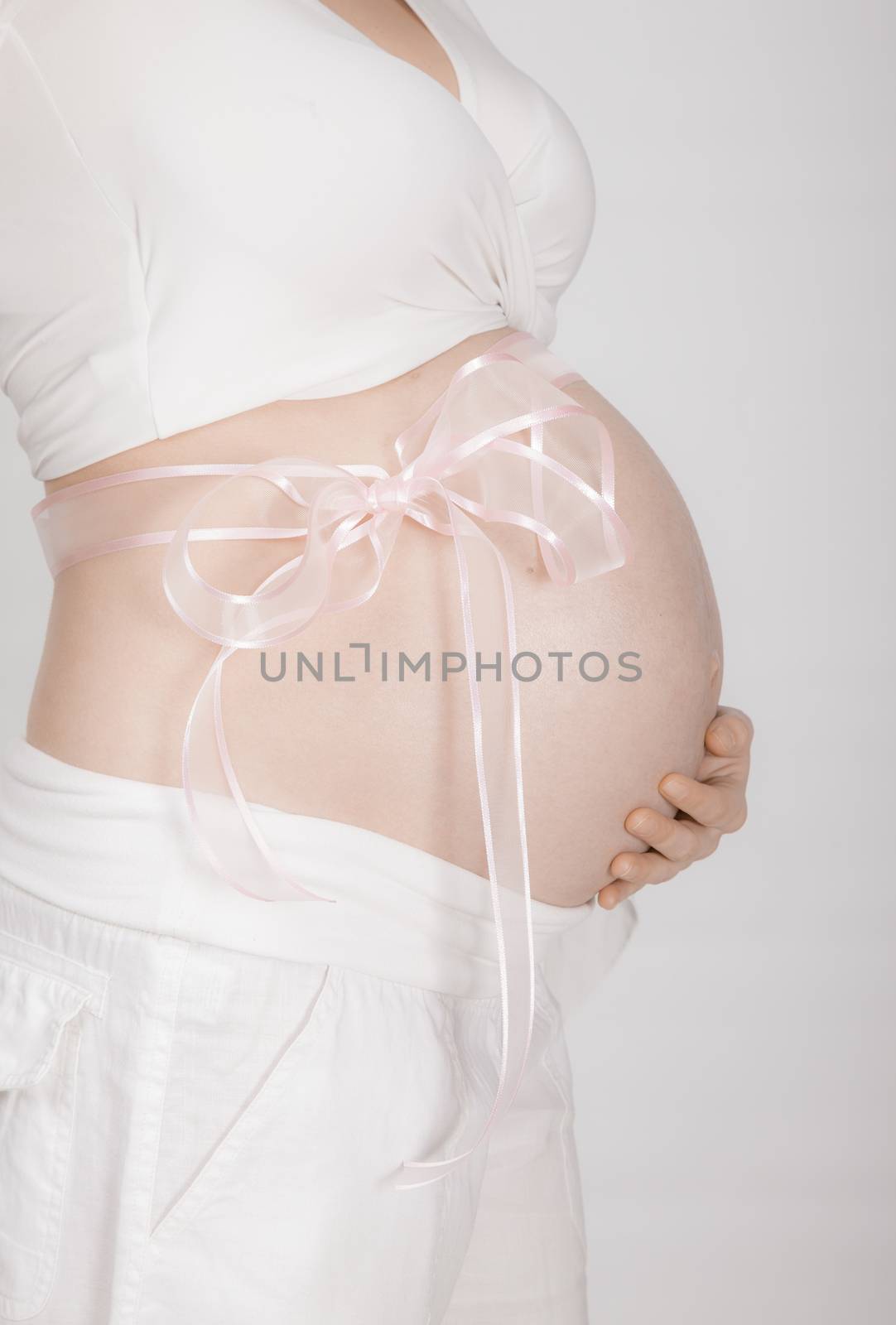 A close-up of a pregnant woman s abdomen, pink ribbon around it, white clothing, high key.