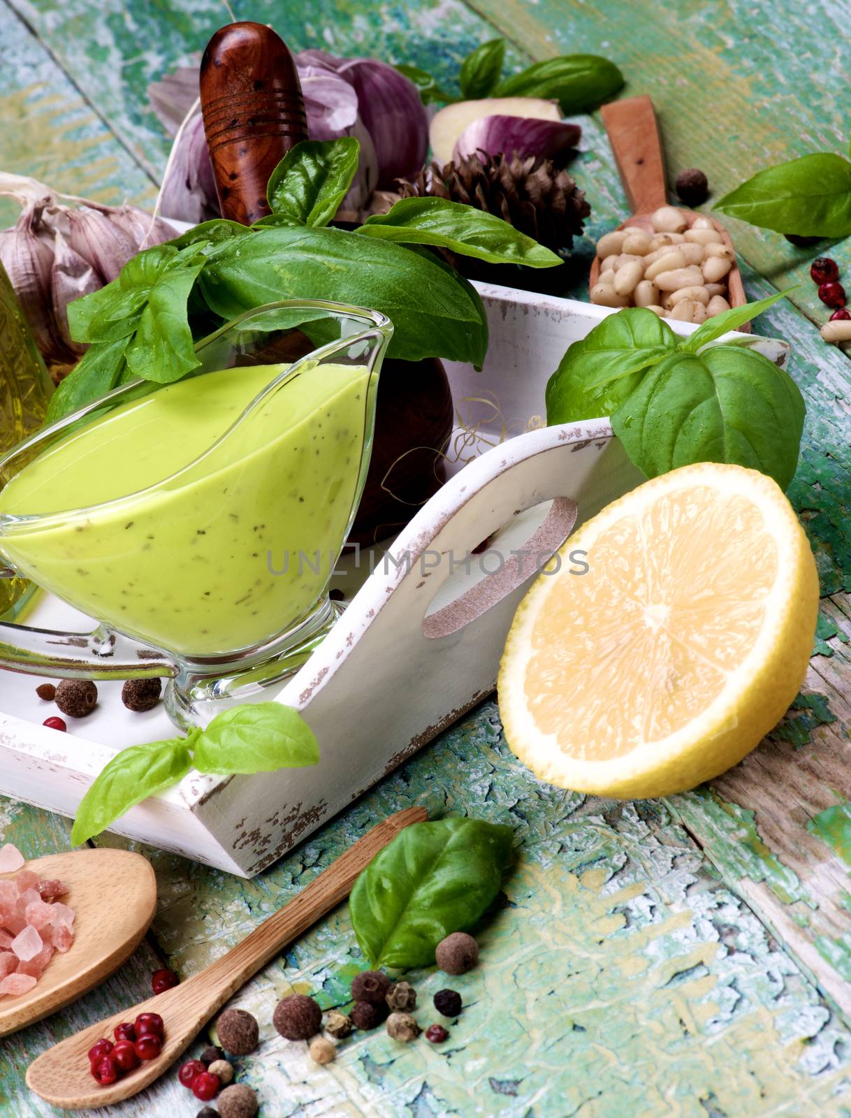 Arrangement of Homemade Freshly Made Creamy Pesto Sauce in Glass Gravy Boat with Ingredients in White Wooden Tray closeup Cracked Wooden background