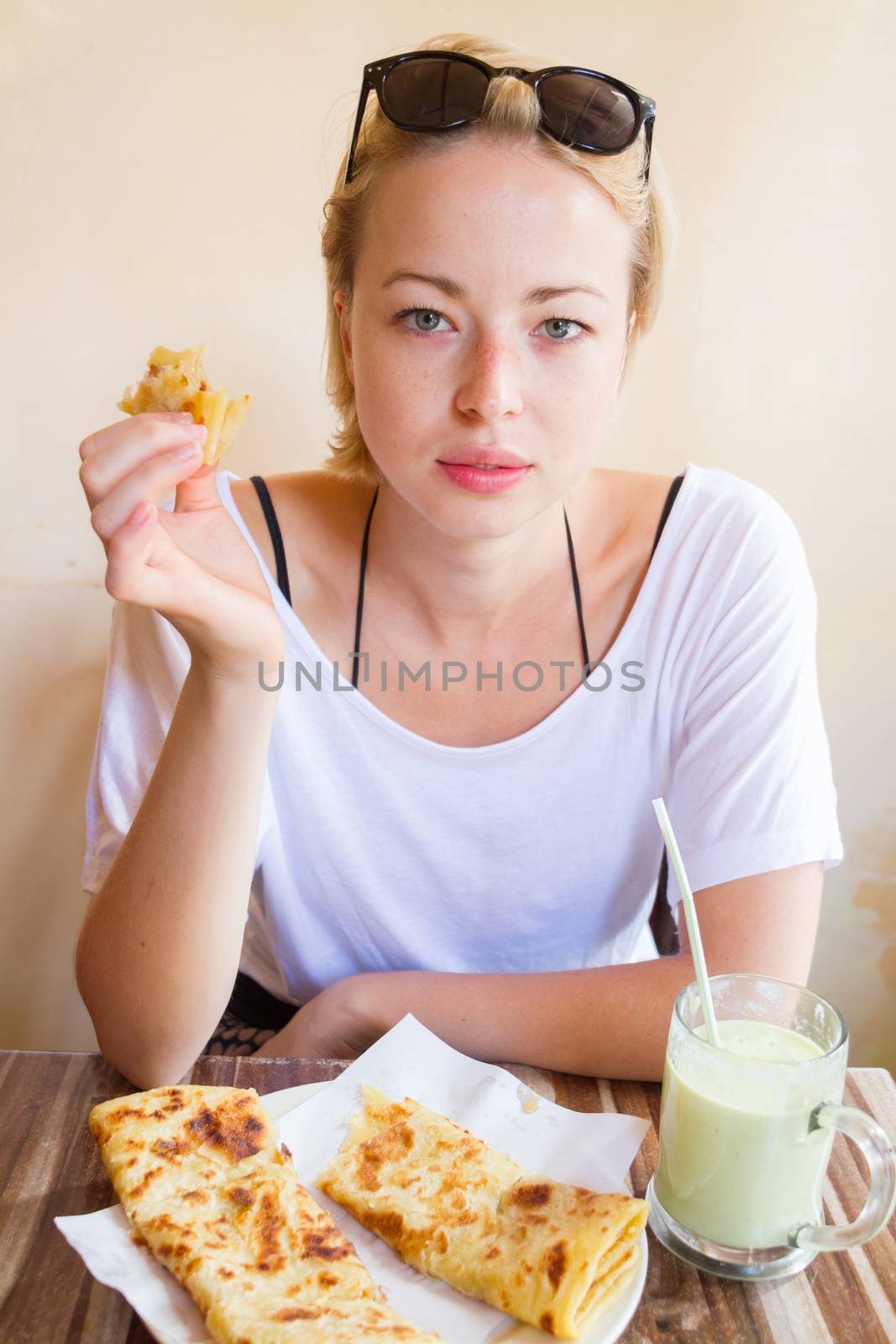 Female tourist eating delicious moroccan brakfast at one of street coffee shops: traditional pancakes with cheese and honey and avocado milkshake.