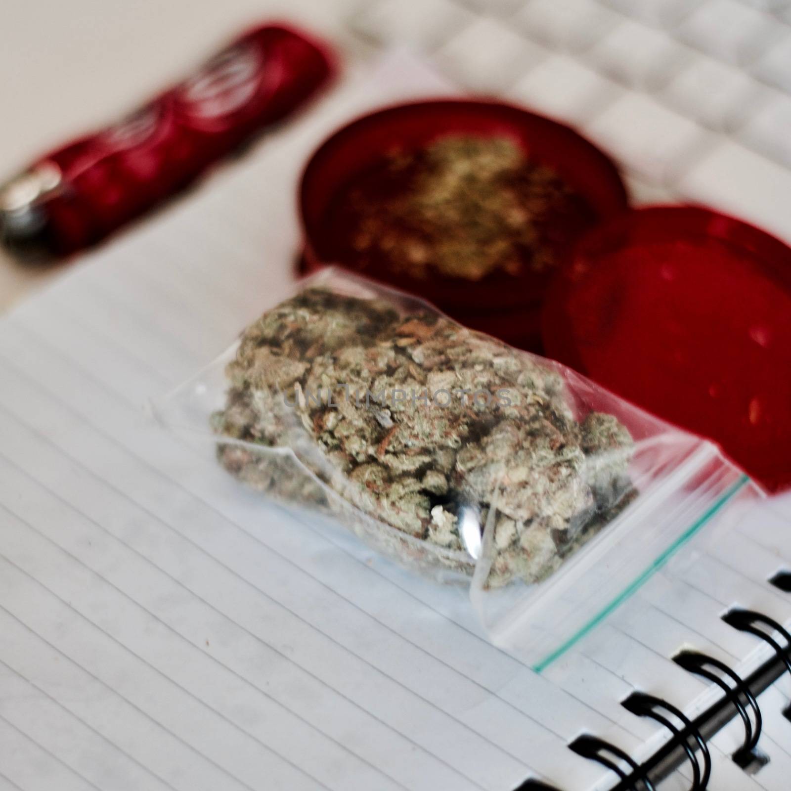 Red grinder, marijuana in big transparent bag near white computer keyboard.