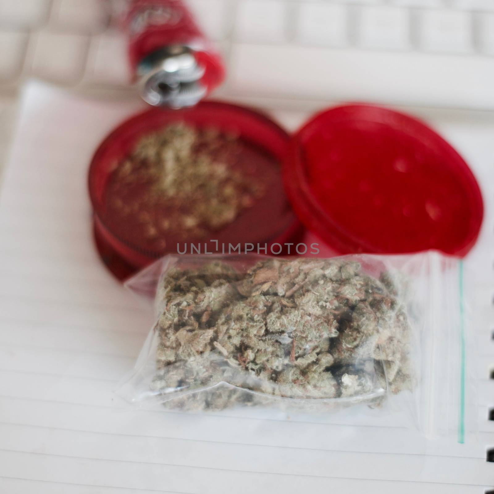 Red grinder, marijuana in big transparent bag near white computer keyboard.