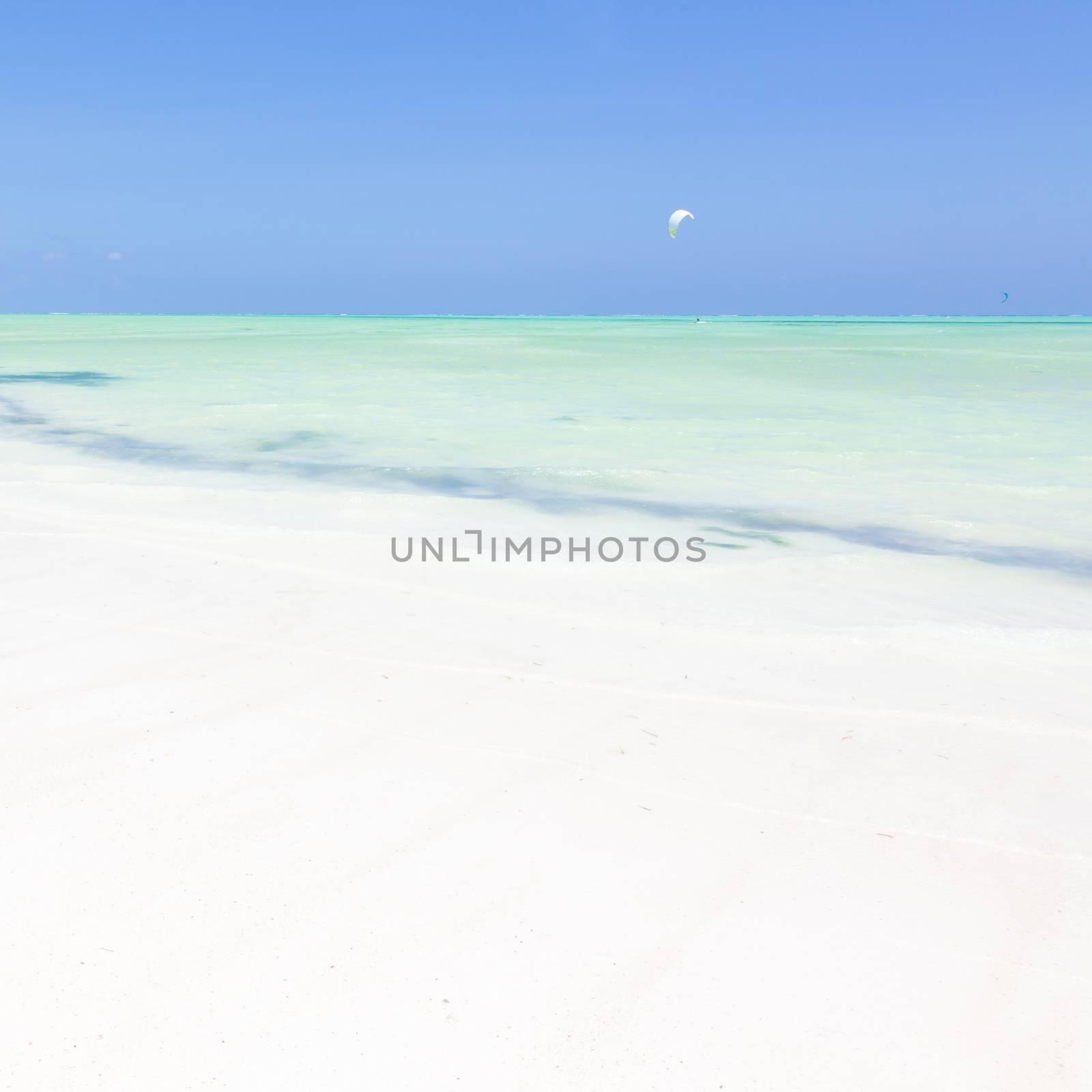 Solitary kite surfer kite surfing on picture perfect white sandy beach with turquoise blue sea, Paje, Zanzibar, Tanzania. Copy space.