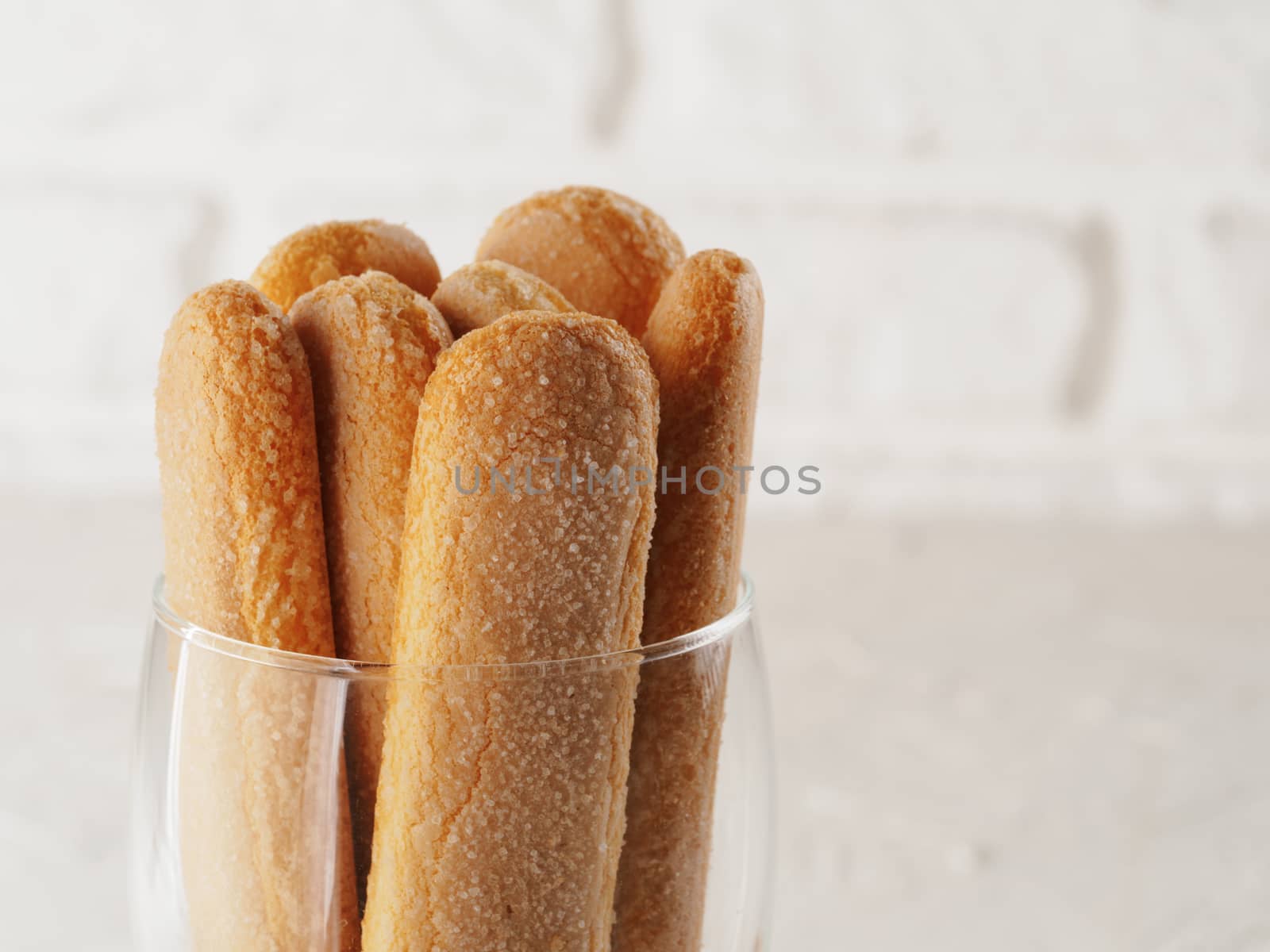 Close up view of ladyfinger biscuit cookie in glass jar on white brick wall background. Italian cookie savoiardi. Copy space.