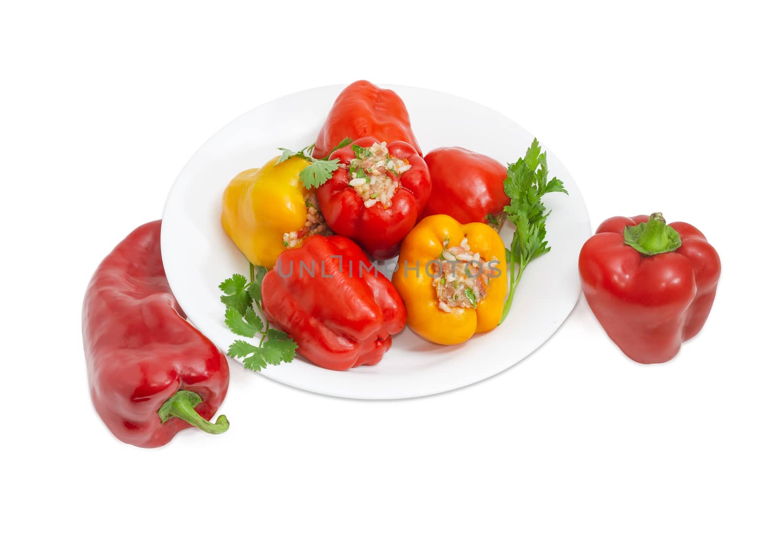 Cooked stuffed red and yellow bell peppers and twigs of parsley and cilantro on a white dish and two uncooked red bell peppers separately beside on a light background
