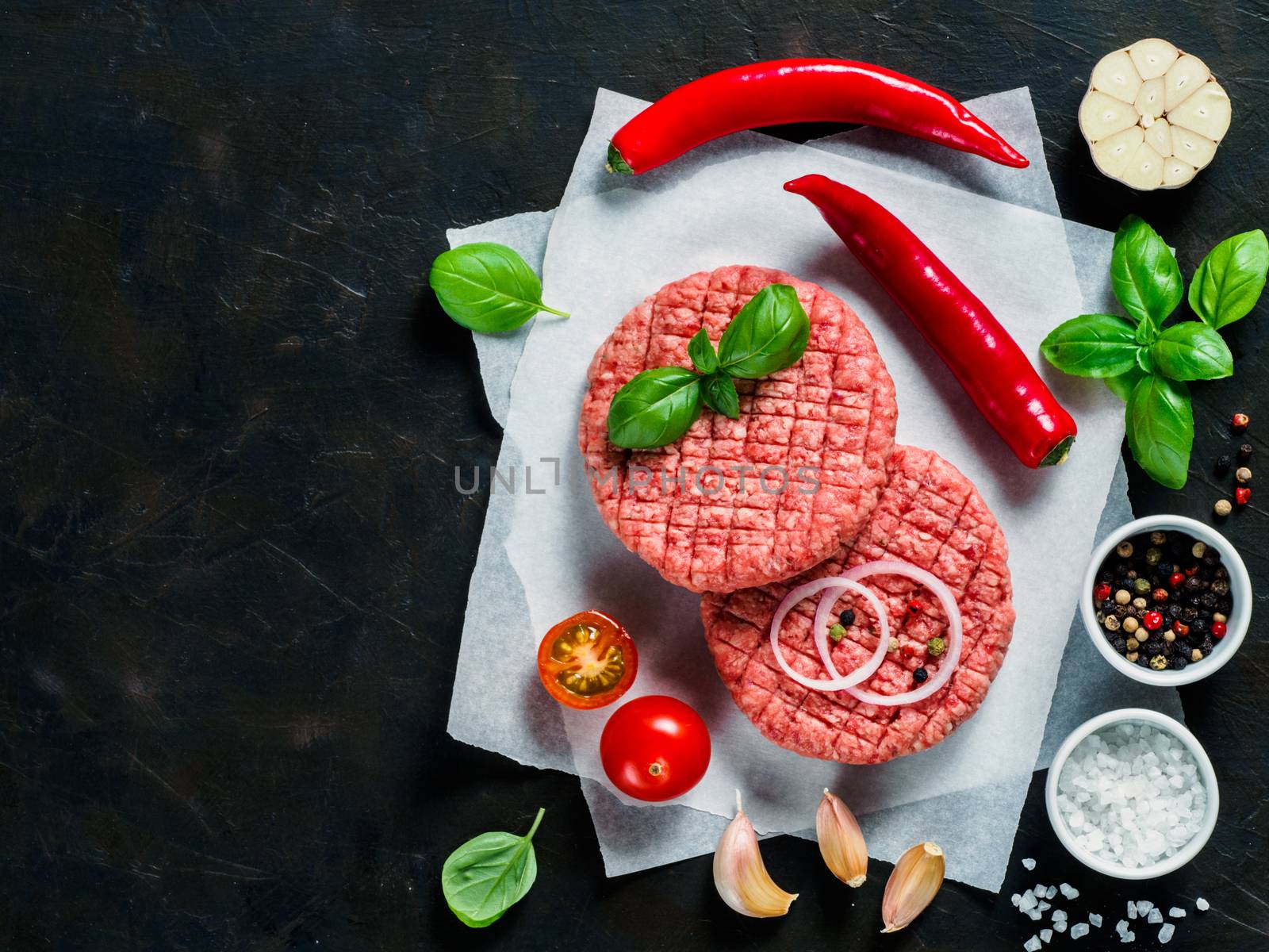 Two raw beef meat steak cutlets for burger with spices and vegetables on black concrete background. Making homemade burger concept. Top view or flat lay. Copy space.