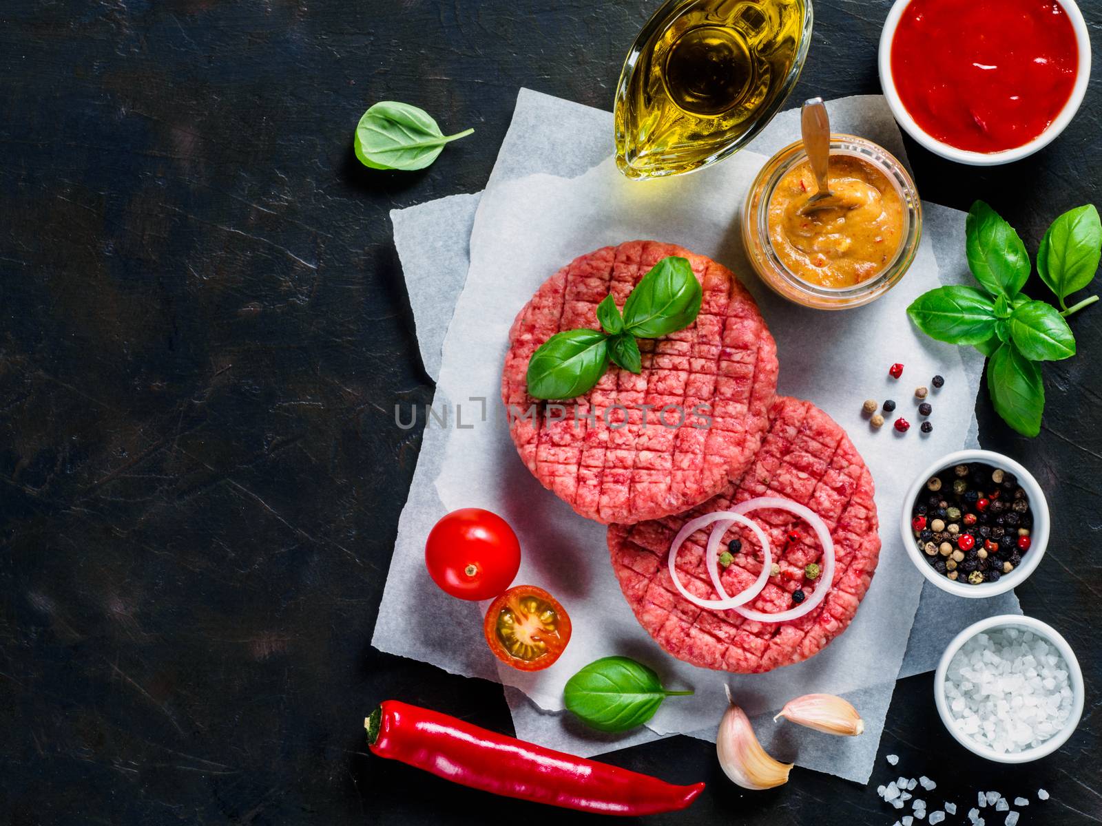 Two raw beef meat steak cutlets for burger with spices and vegetables on black concrete background. Making homemade burger concept. Top view or flat lay. Copy space.