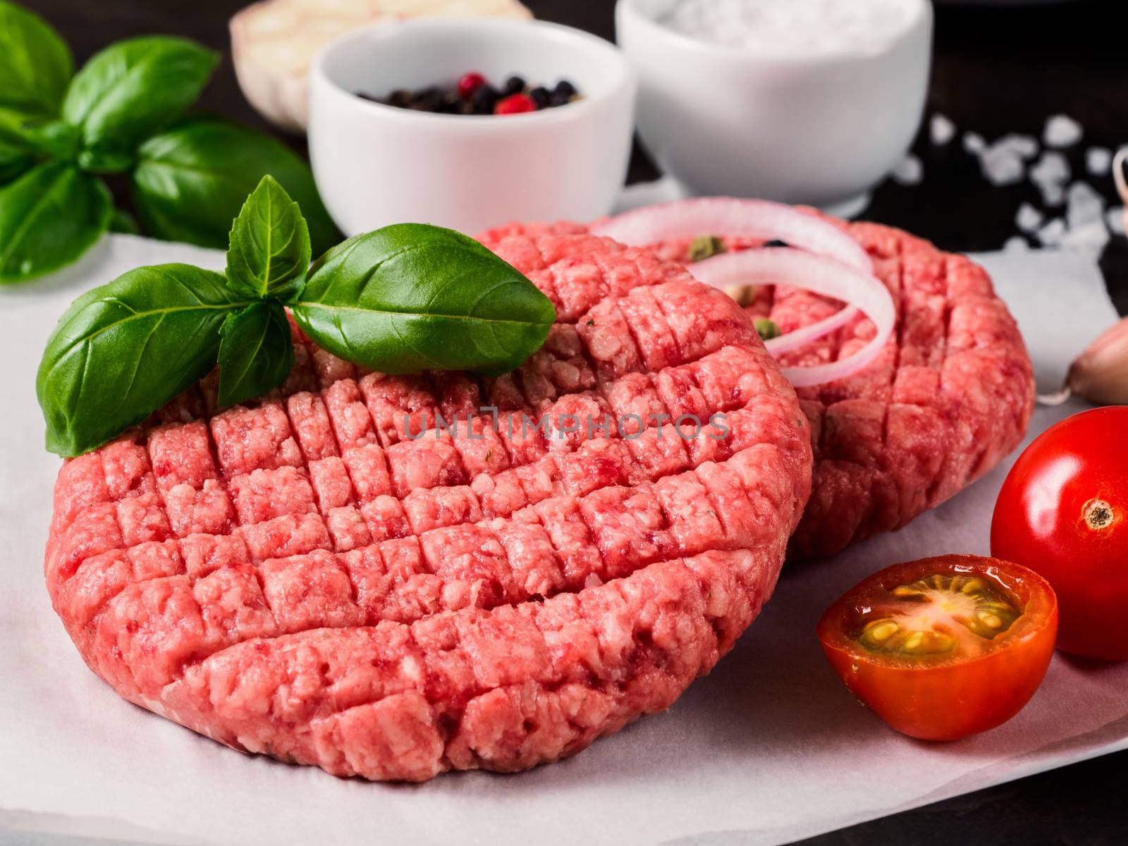 Close up view of two raw meat steak cutlets for burger with vegetables, spices and fresh basil. Making homemade burger.