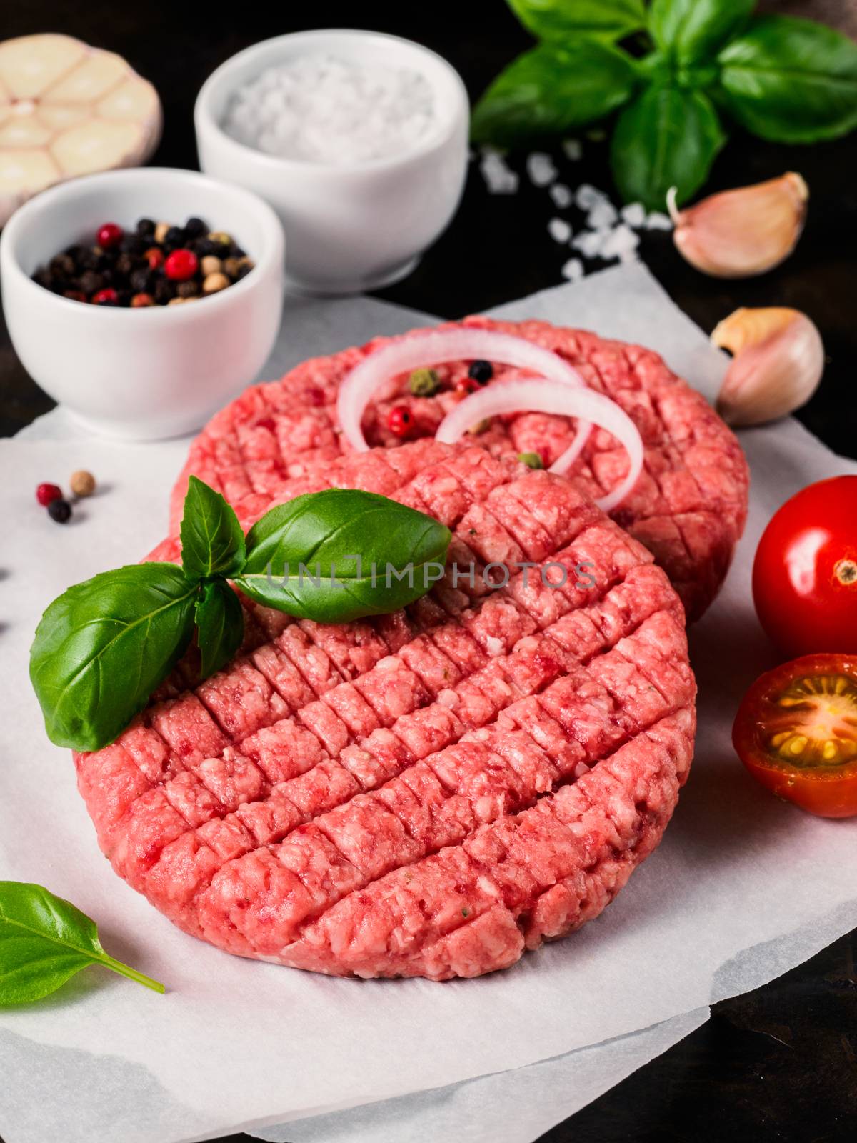 Close up view of two raw meat steak cutlets for burger with vegetables, spices and fresh basil. Making homemade burger. Vertical.