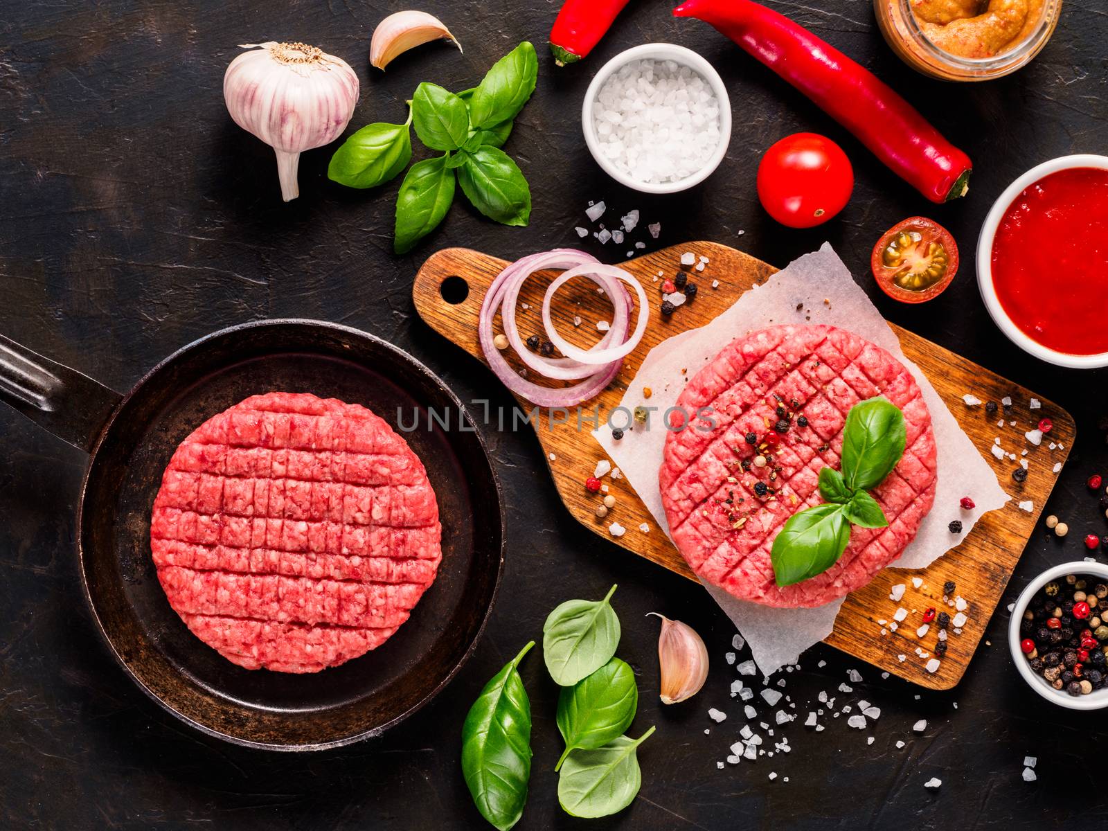 Raw beef meat steak cutlet for burger in pan, cutlet on wooden cutting board with spices, vegetables,sauces ketchup and mustard on black concrete background.Making homemade burger.Top view or flat lay