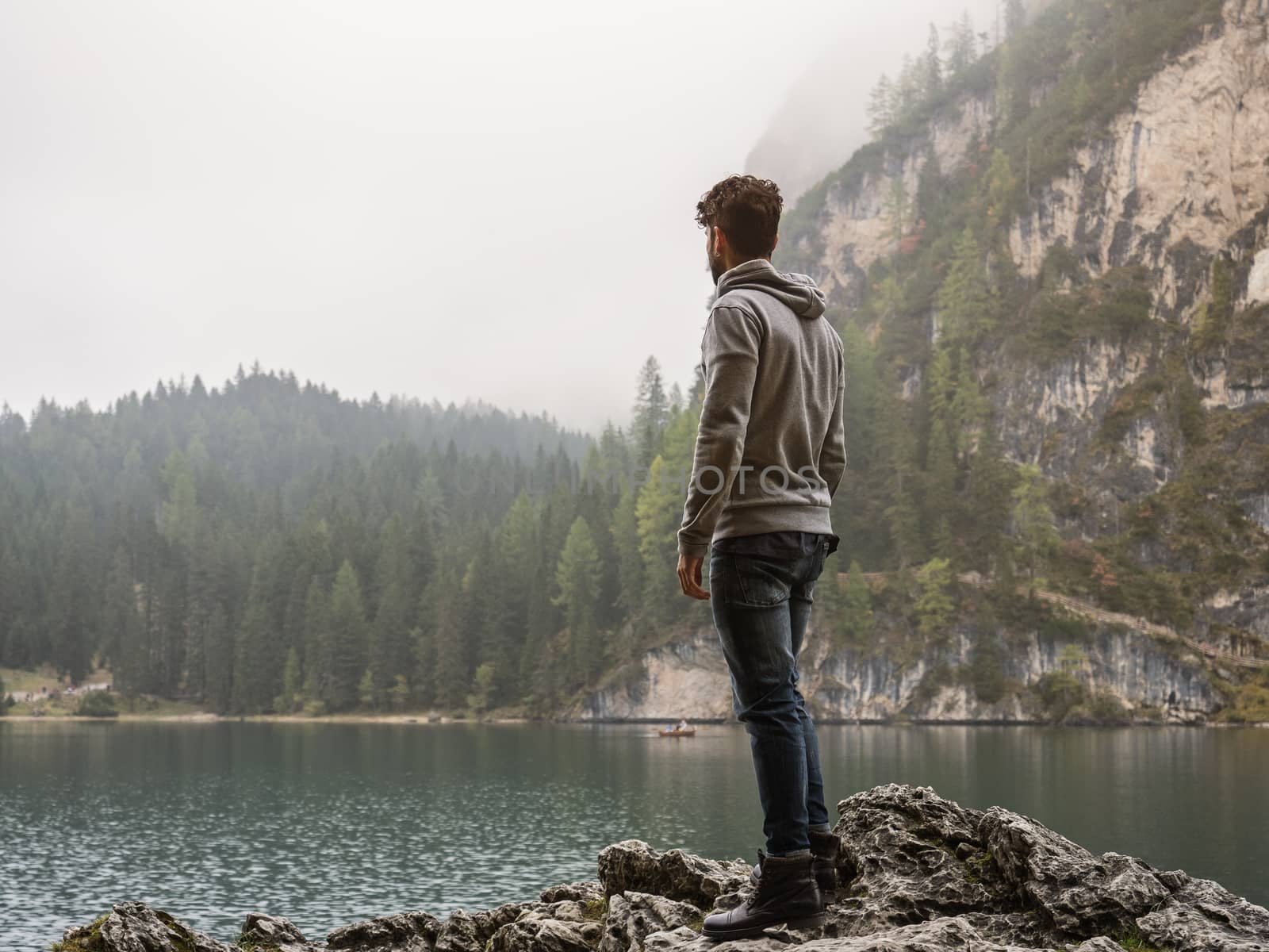 Handsome yung man standing on background of woods on shore of lake looking away.