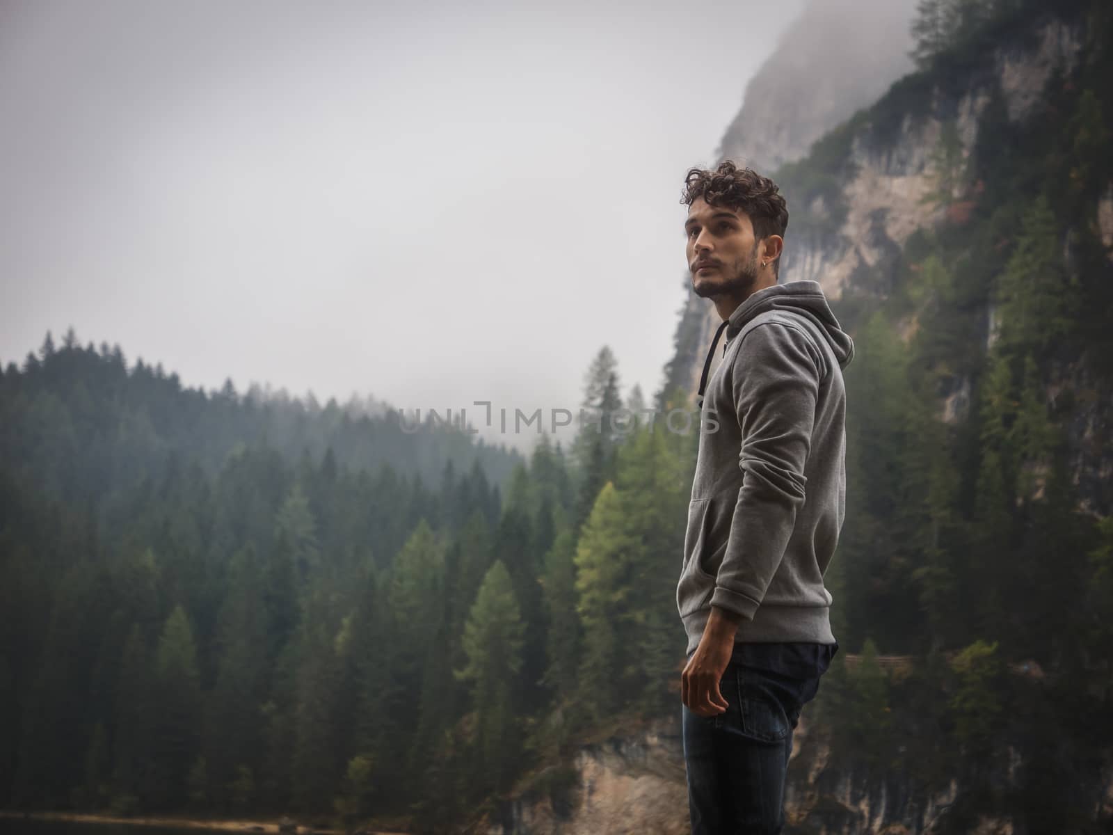 Handsome yung man standing on background of woods looking away.