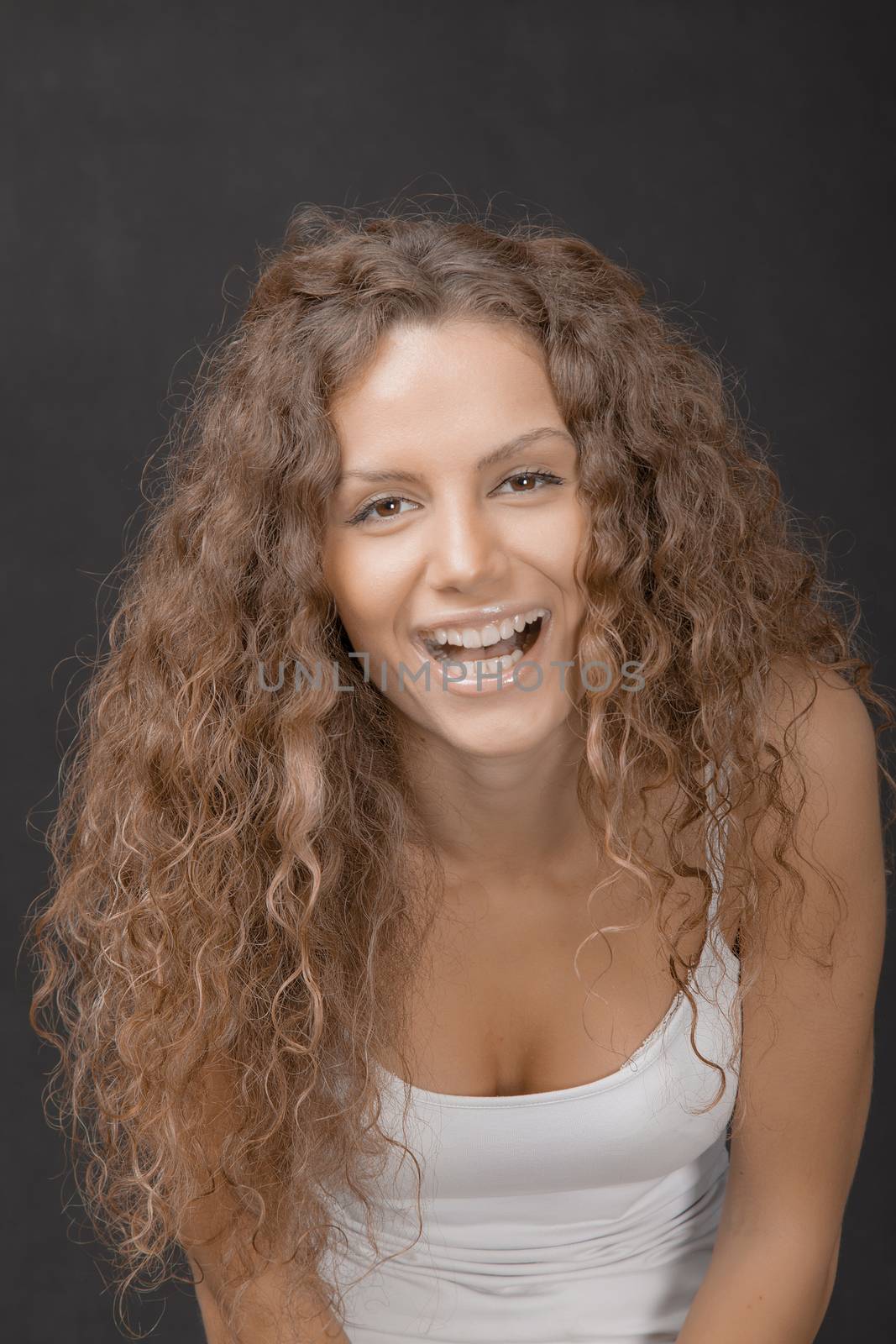 A young beautiful female with gorgeous hair laughing to camera. Studio shot.