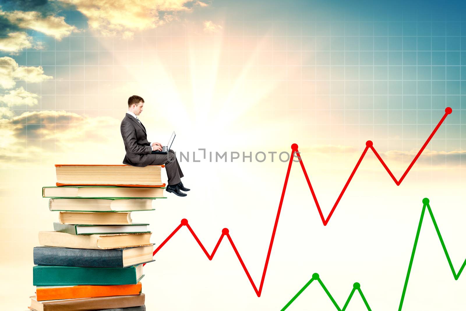 Young man sitting on a stack of books with a laptop, sky background
