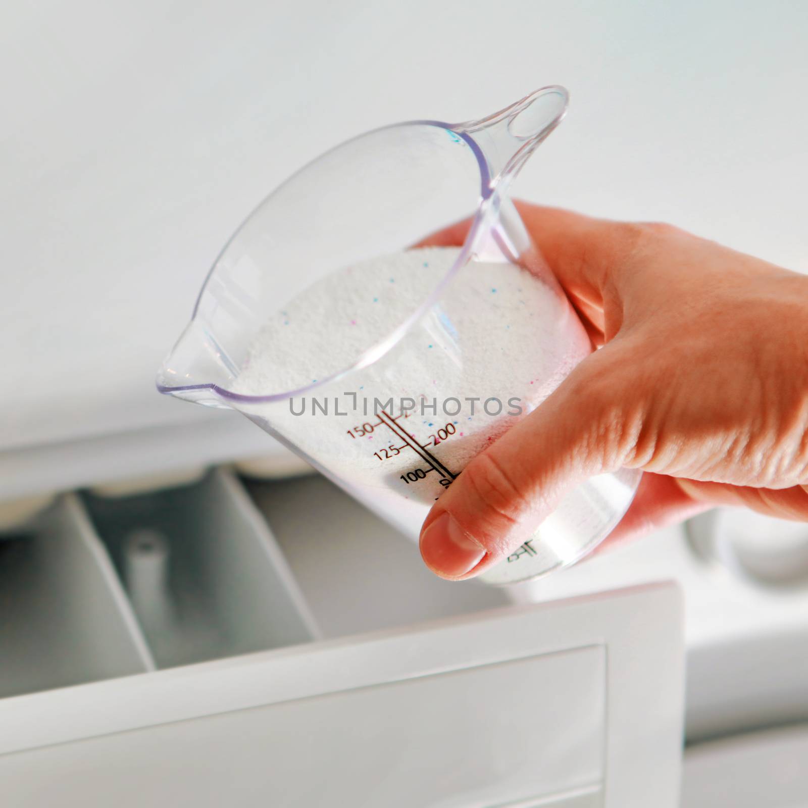 hand of woman that fills detergent from dosing cup in the washing machine