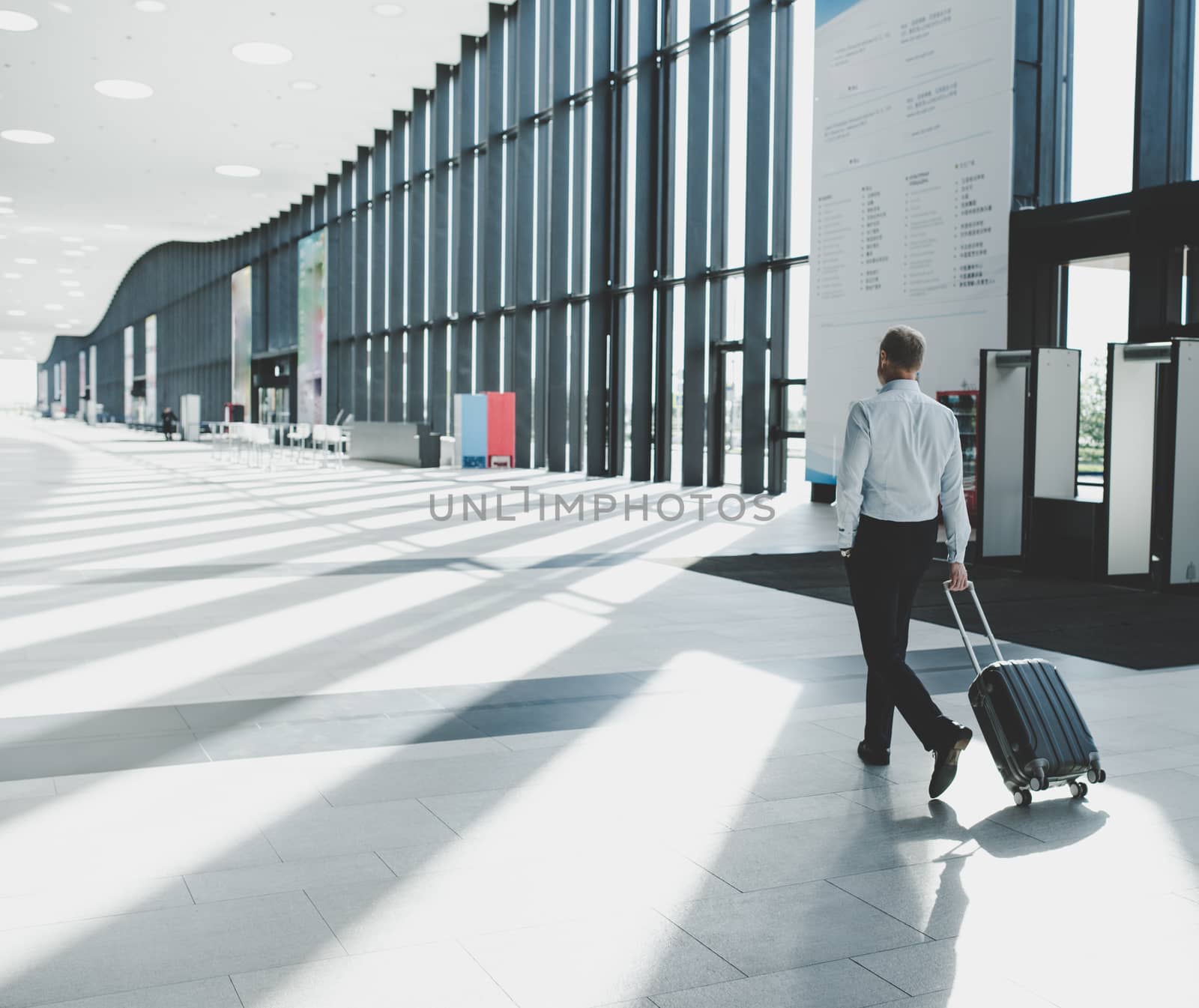 Business man in formal clothing walking with wheeled bag at airport terminal