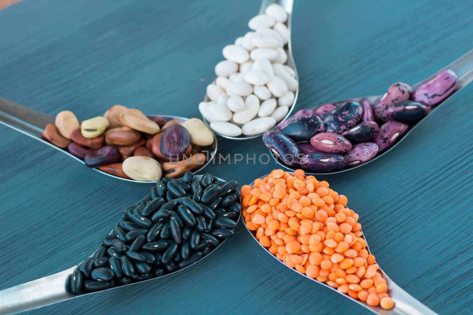 Yellow lentils, black, white, brown, purple kidney beans on metal spoons star composition on blue wooden background