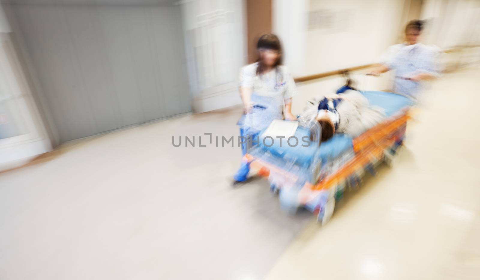 An emergency litter with patient, pushed fast through modern hospital corridor by two nurses. Panned, motion blurred picture.