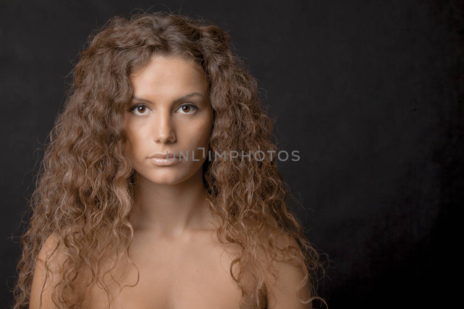 A beauty shot of a pretty young female with gorgeous curly long hair, low key.