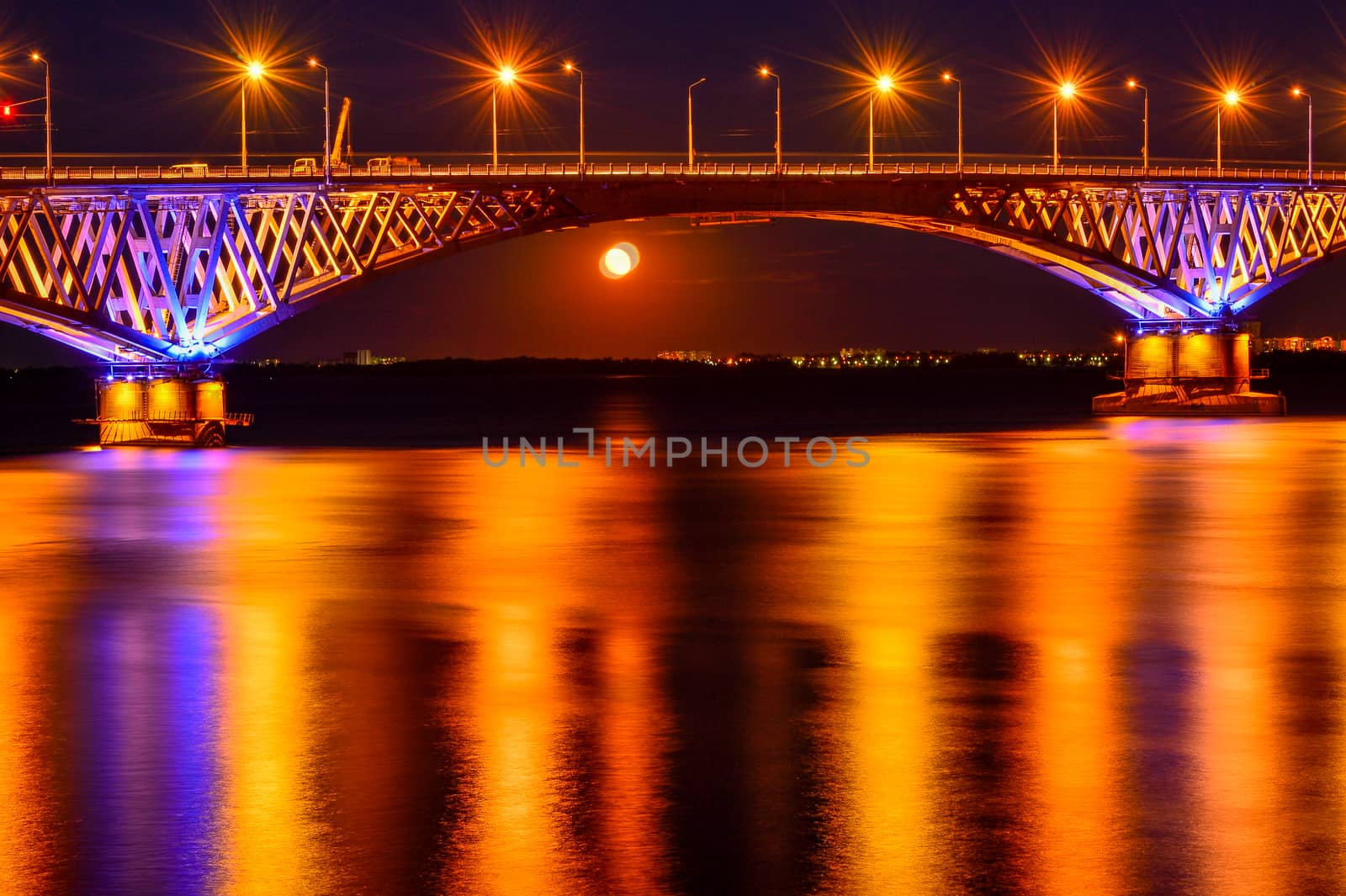Bright night lights of a large bridge across the river are reflected in the water.