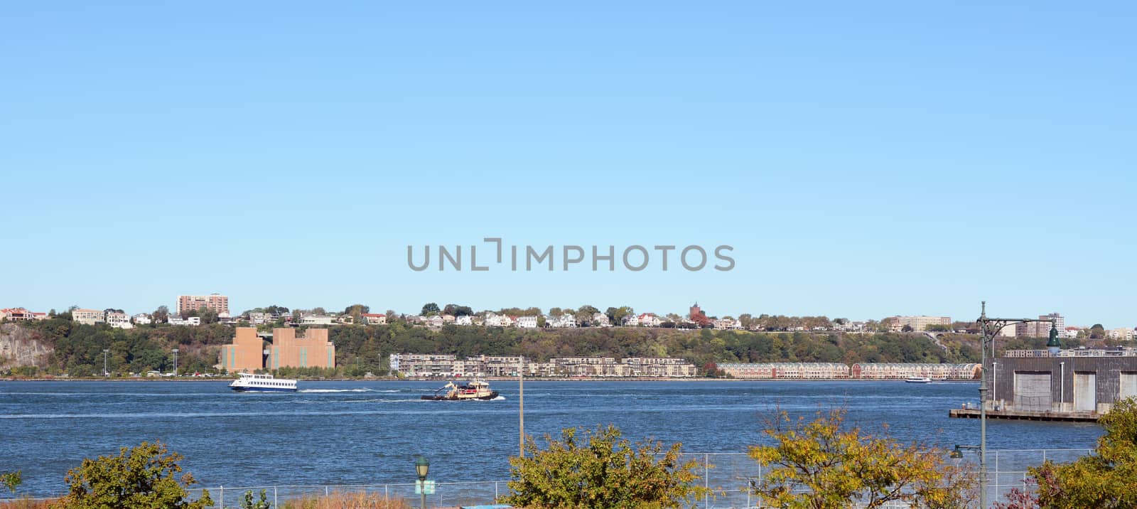 Ferry and work boat navigate the Hudson River in New York City. Weehawken and Hamilton Park in New Jersey are on the opposite riverbank.