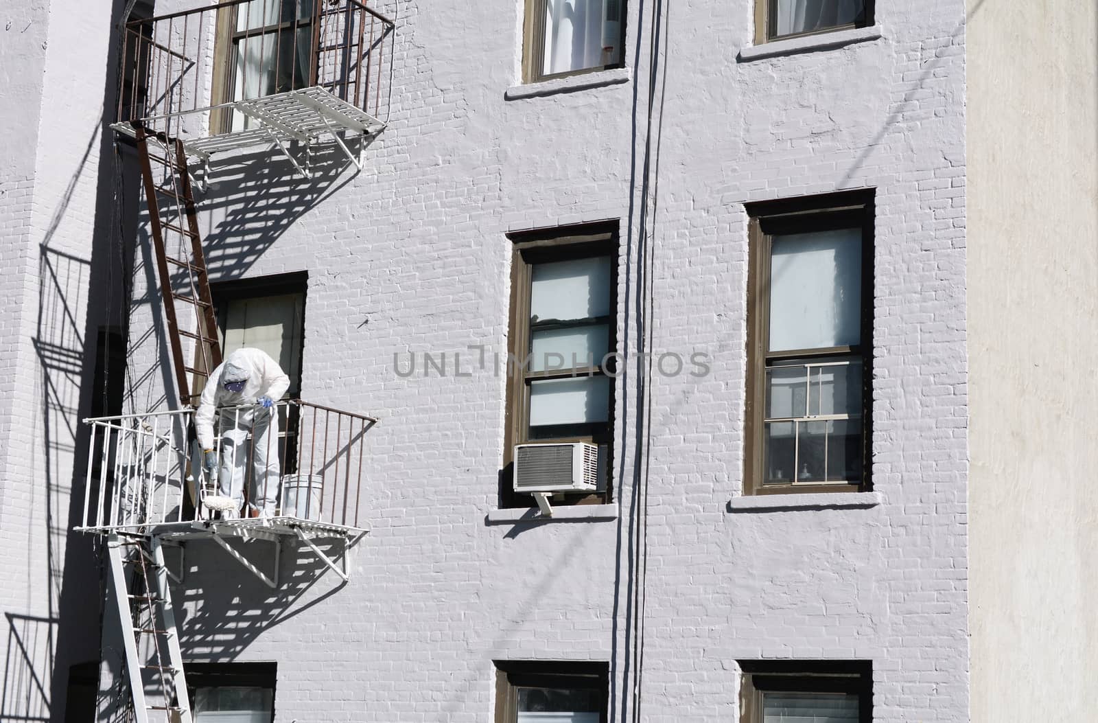 Painter dressed in coveralls, painting metal fire escape white on an apartment building in New York City
