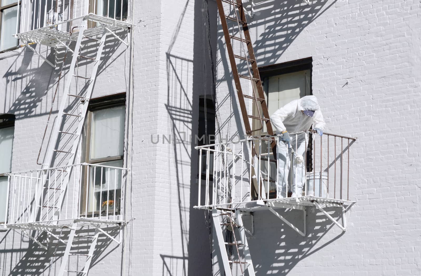 Building painter, dressed in protective overalls, painting metal fire escapes white at the rear of a building in Manhattan, New York City