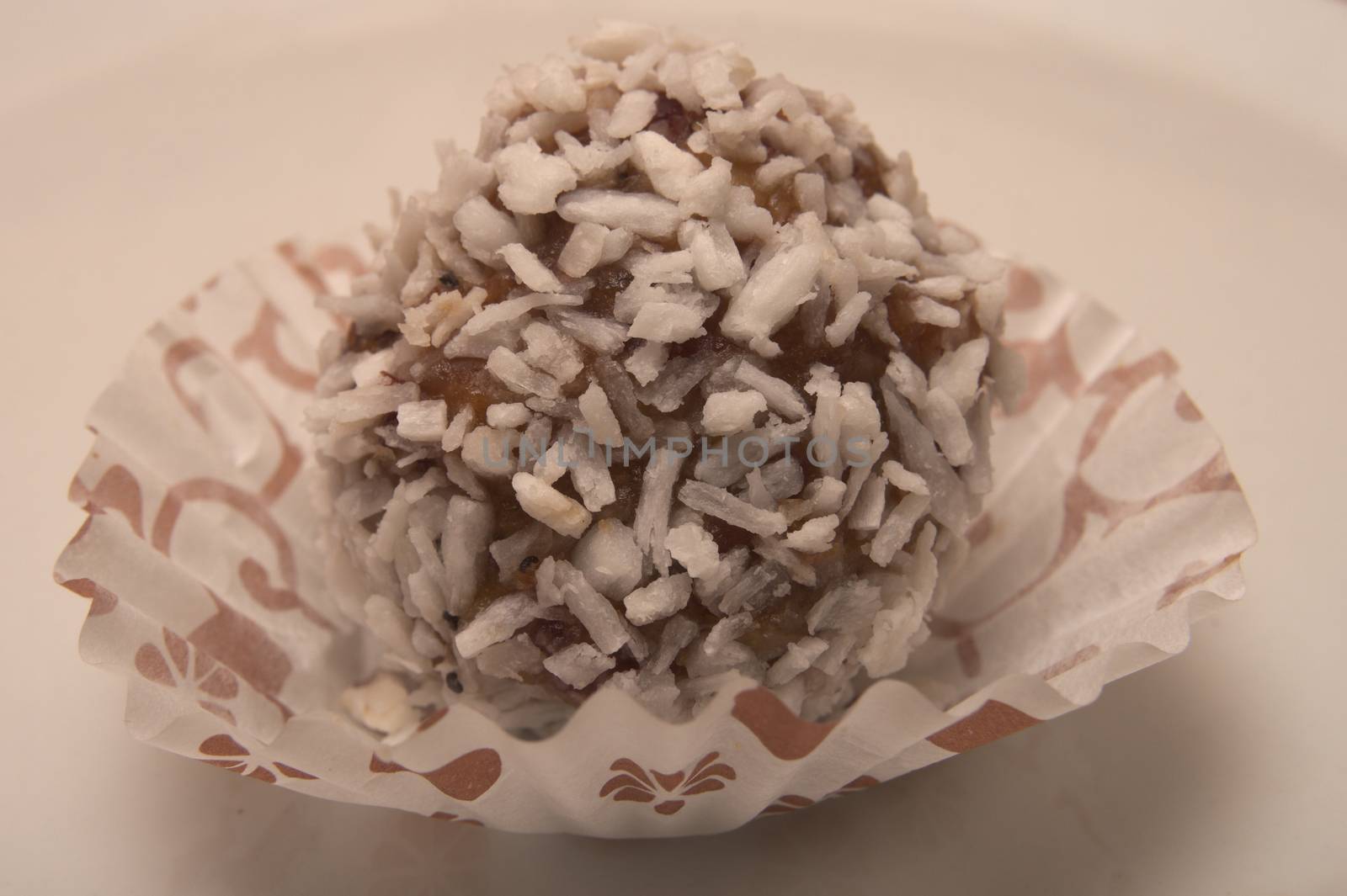 One small sweet round decert made from chocolate, covered with white coconut shavings placed in paper wrapper