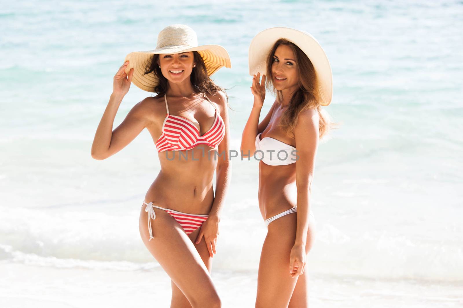 Happy smiling female friends in bikini and sunhats on vacation