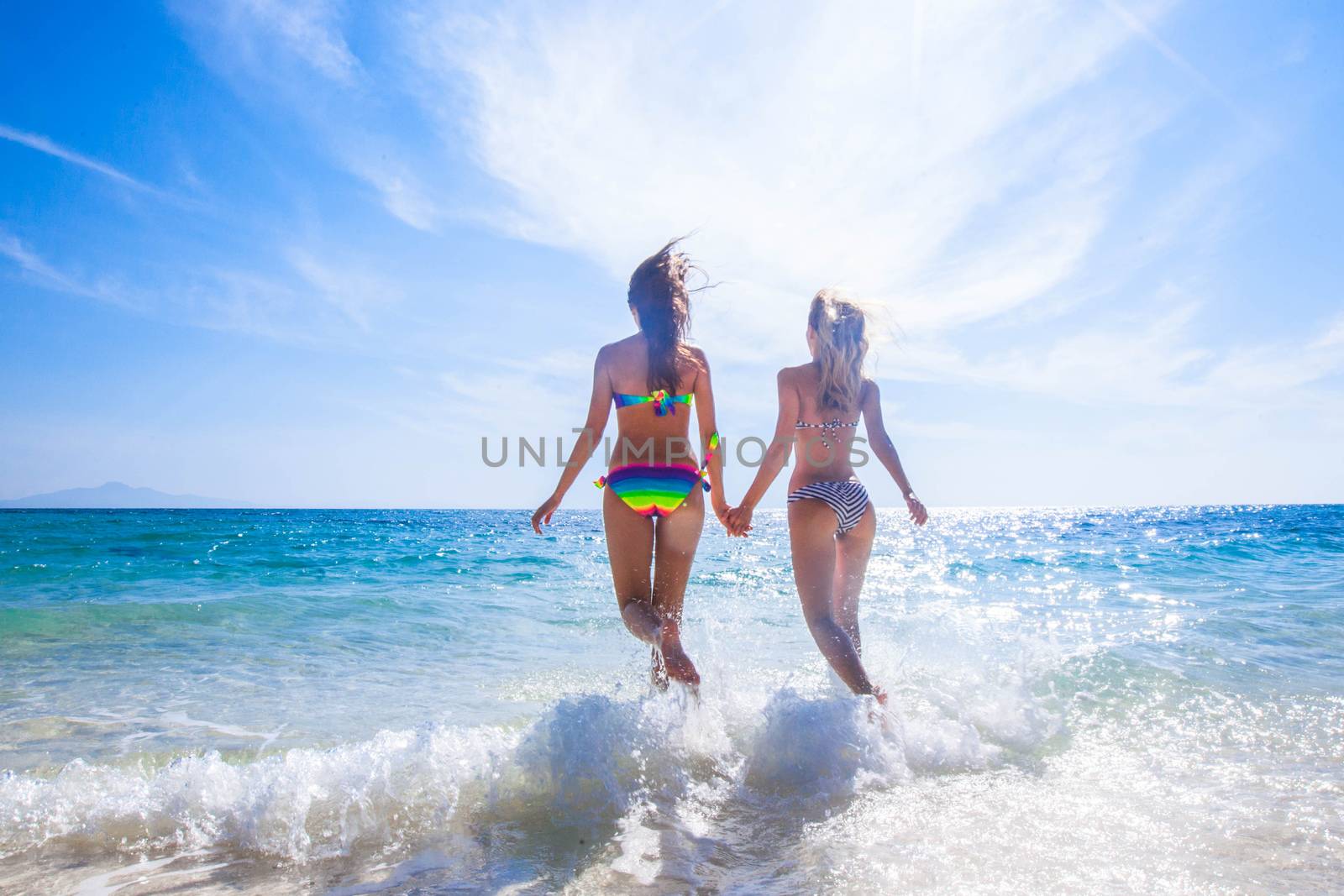 Two young and attractive women in bikini running by the beach