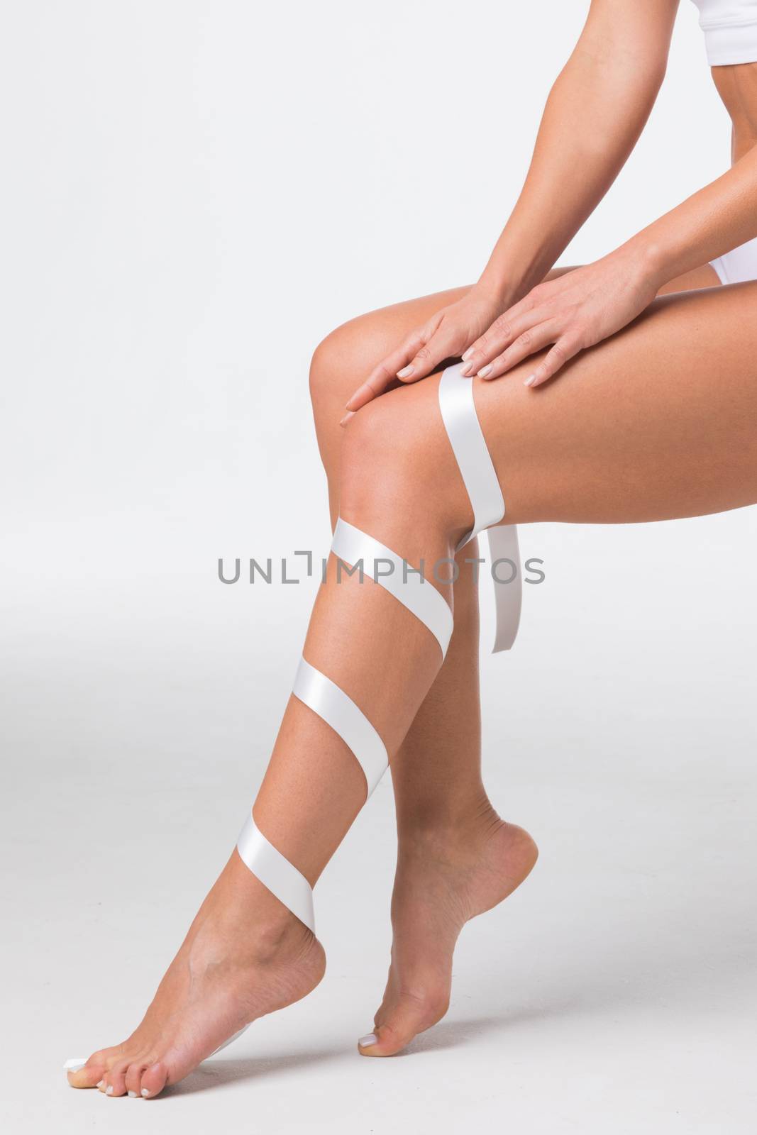 Studio shot of young woman with perfect body with leg wrapped in white ribbon, depilation, varicose concept