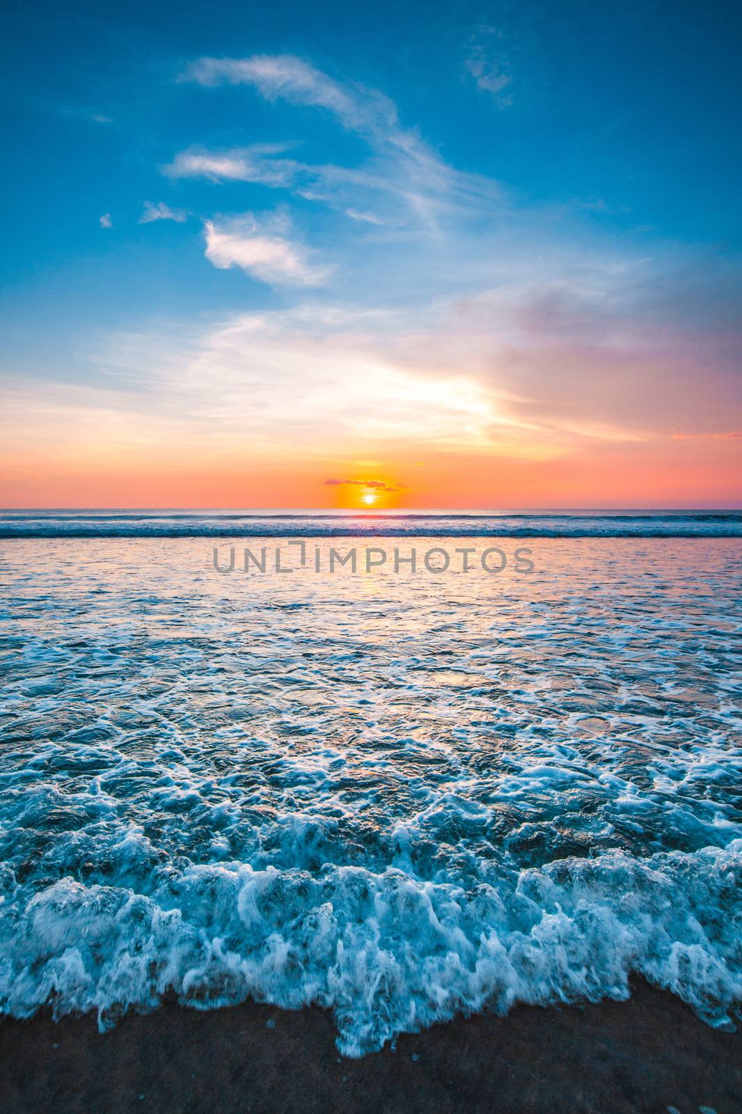 Splashing ocean wave in front of beautiful sunset sky background